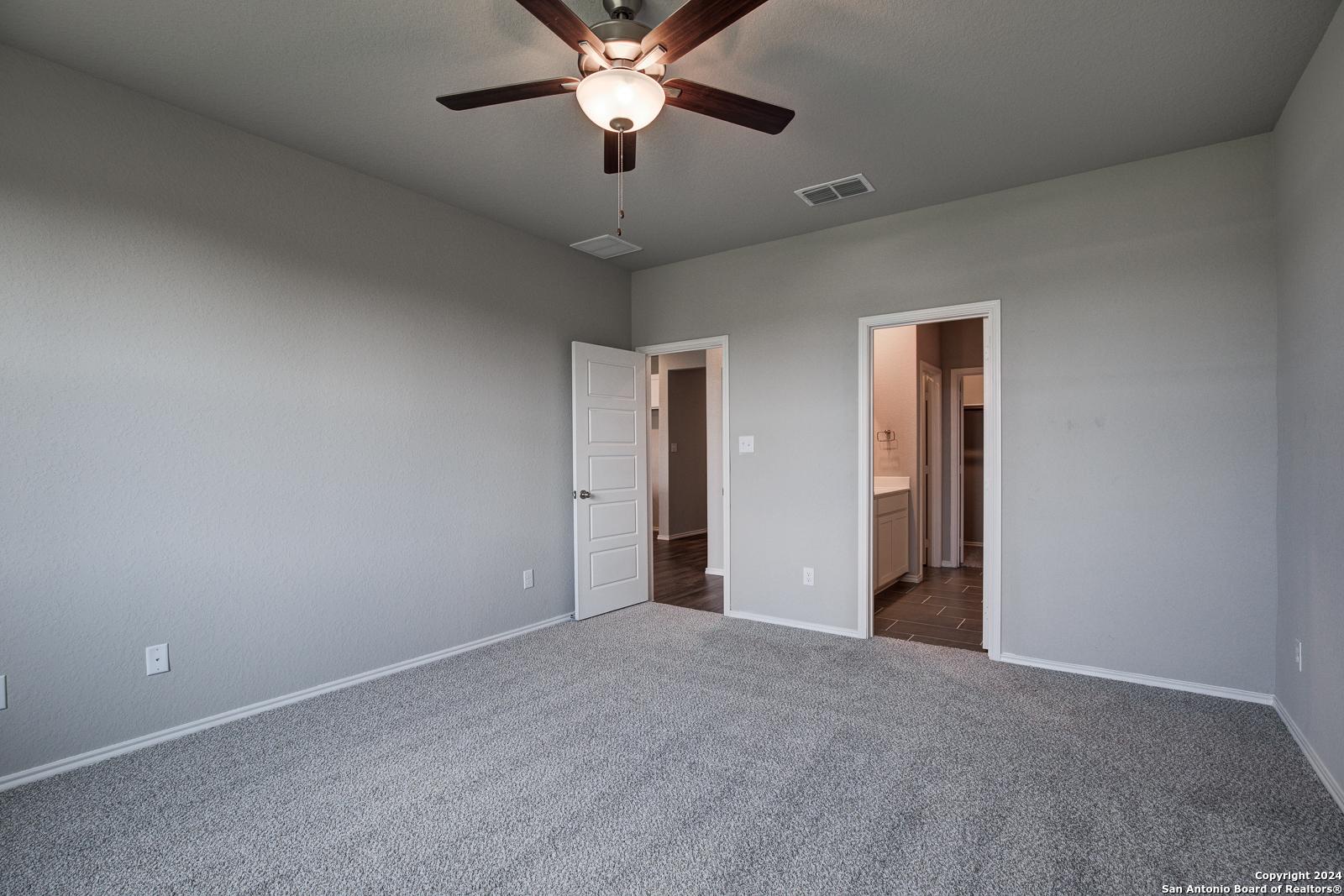 Neutral gray secondary bedroom with ceiling fan, carpet floor, and attached bath vanity in Davidson Homes The Daphne J, Seguin, Texas