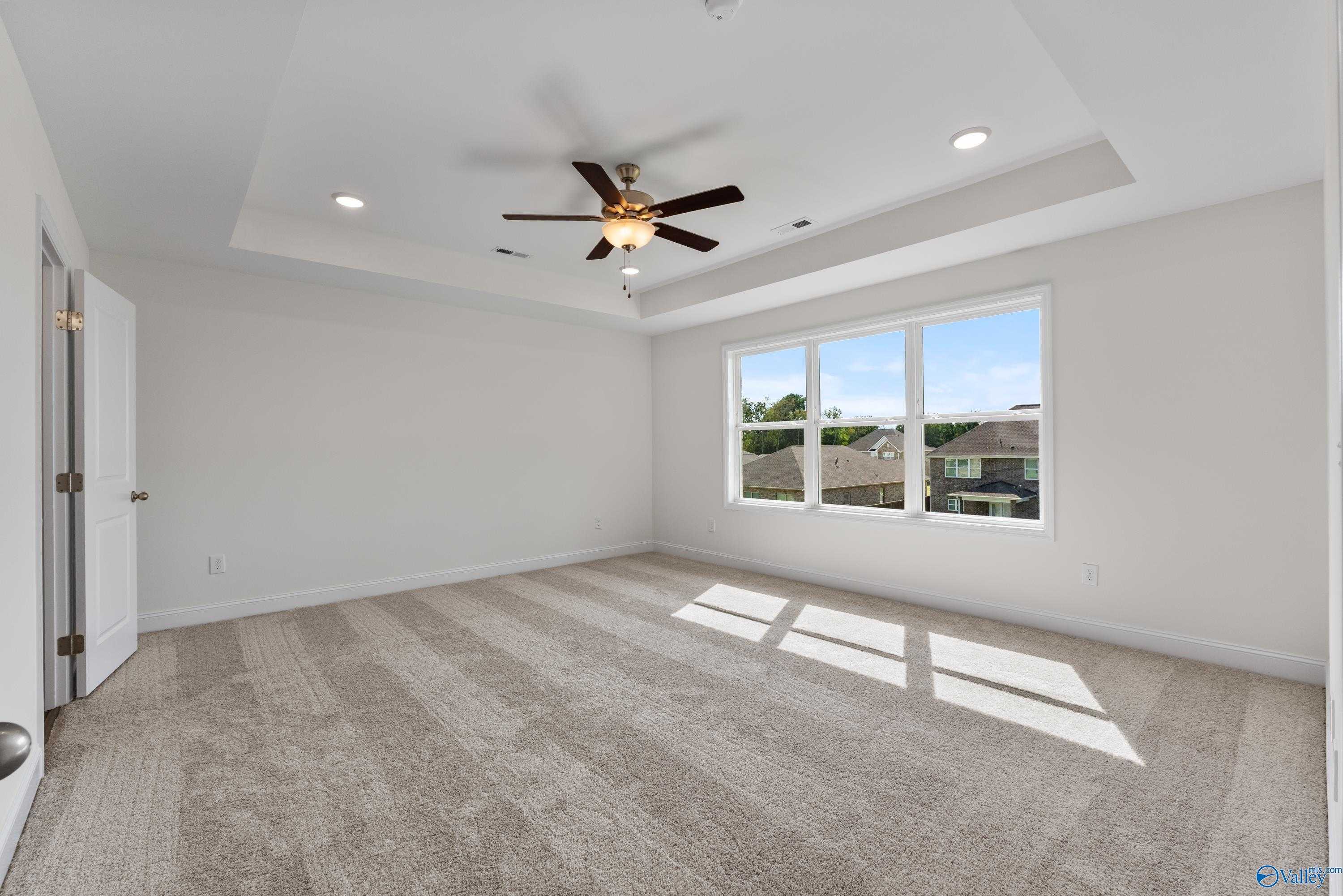 Bright empty bedroom featuring tray ceiling, ceiling fan, and large windows with neighborhood view in Davidson Homes The Shelby A, New Market, Alabama