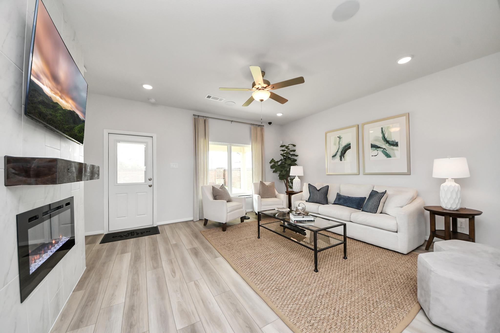 Bright living room in Sunterra by Davidson Homes, Katy, Texas, featuring a marble fireplace, white sofa, and wood floors.