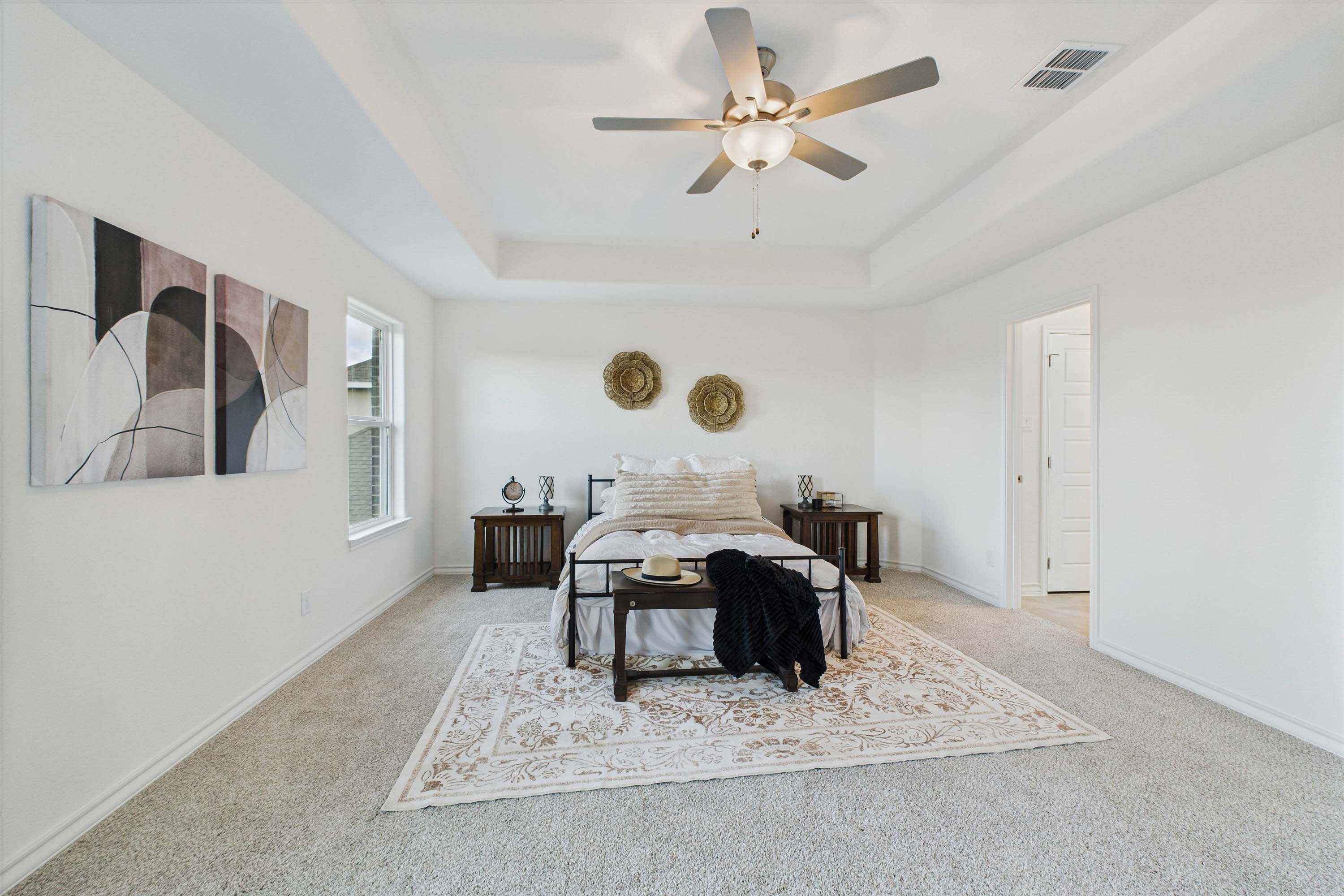 Spacious master suite in The Danbury I featuring a tray ceiling, plush carpeting, and elegant bedroom decor.