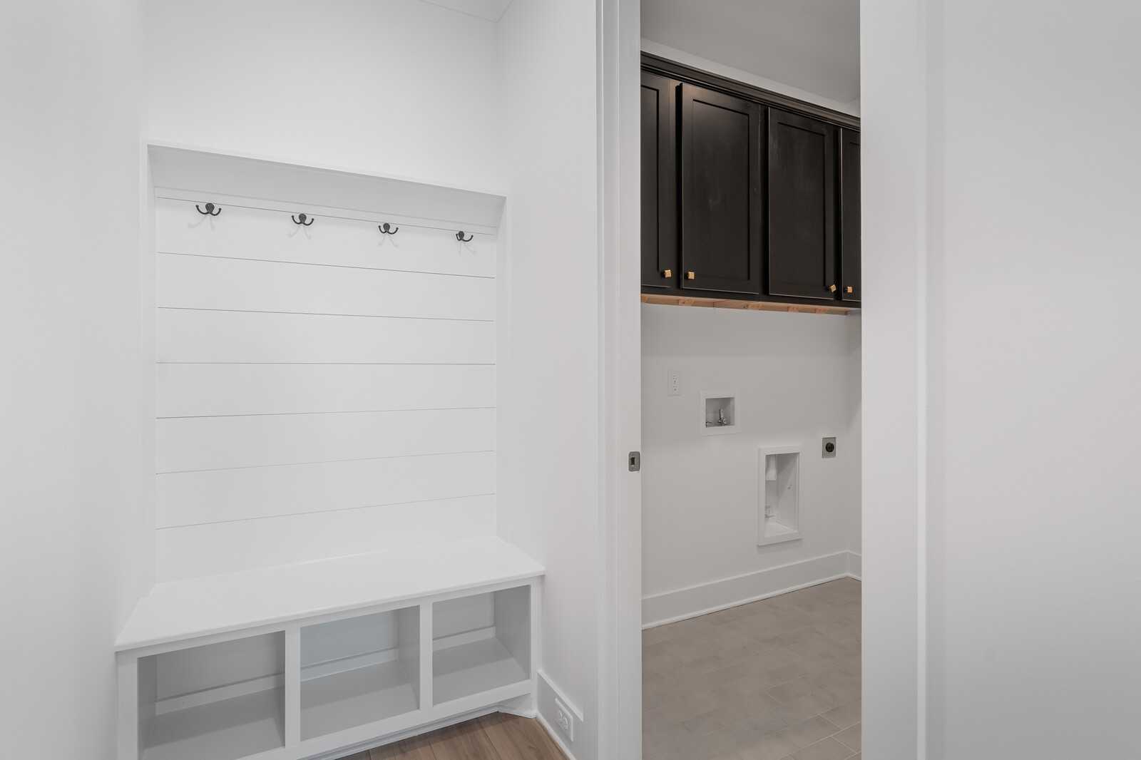 Spacious mudroom with white shiplap walls, coat hooks, built-in bench and adjacent laundry room in Davidson Homes The Hathaway, Murfreesboro