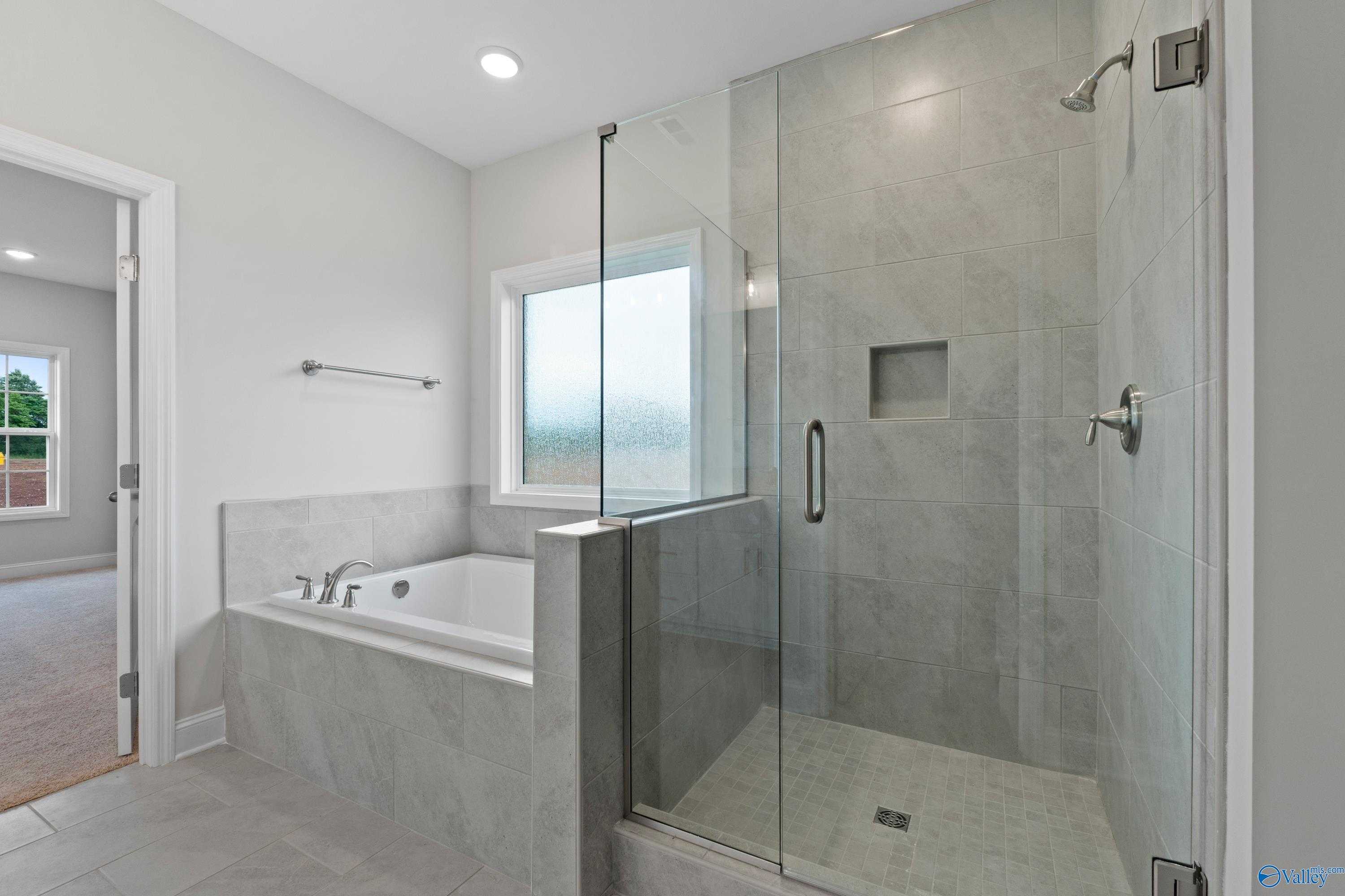 Modern master bathroom featuring frameless glass shower, soaking tub, and tiled walls in Davidson Homes The Rockford B, Toney, Alabama