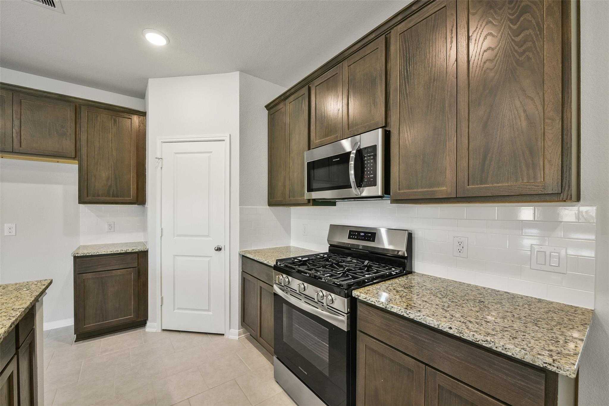Modern kitchen featuring warm wood shaker cabinets, granite countertops, stainless steel appliances in The Sabine E by Davidson Homes, Dayton, Texas