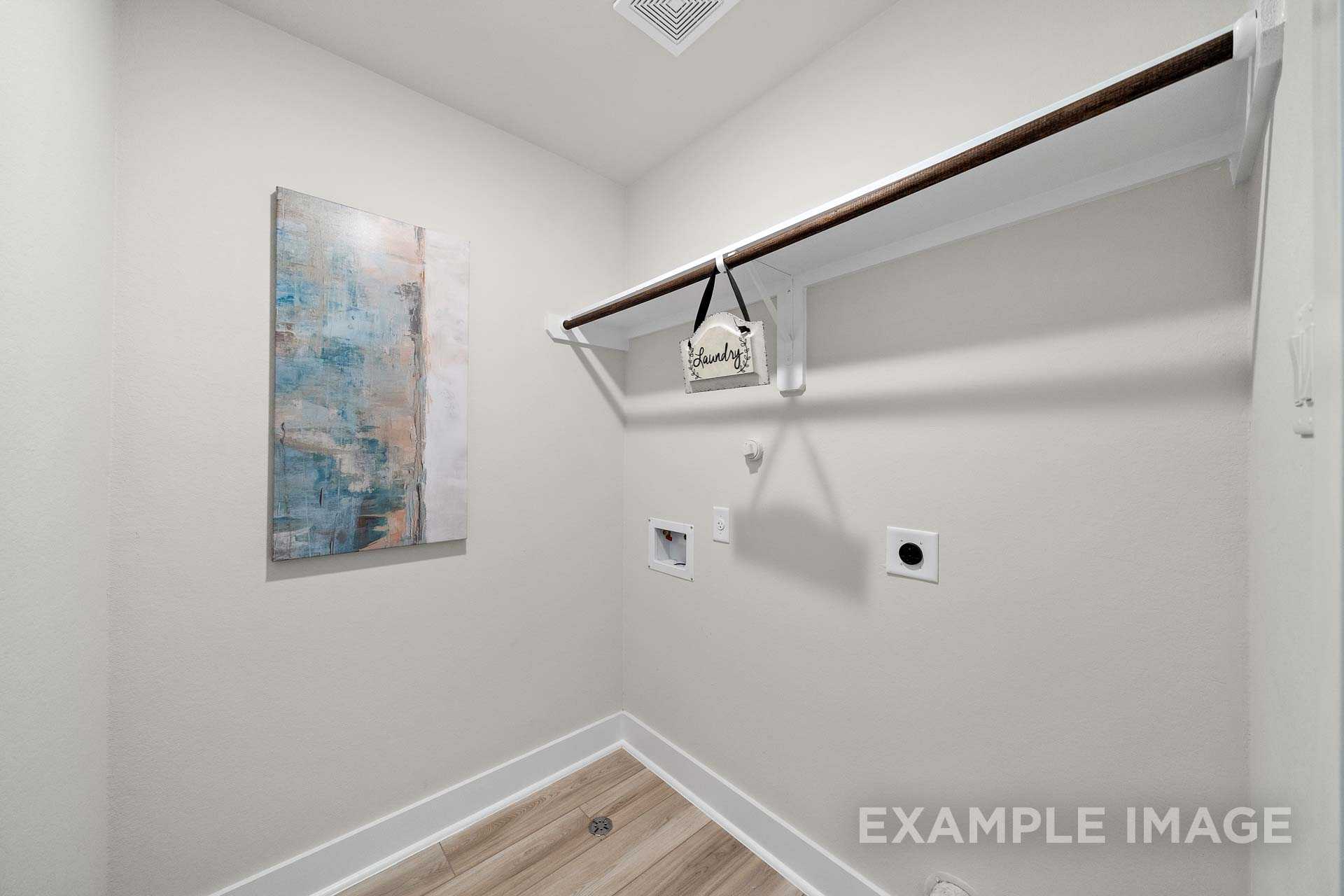 Spacious laundry room in The Lily A by Davidson Homes, featuring wooden shelf, abstract art, utility hookups and outlets