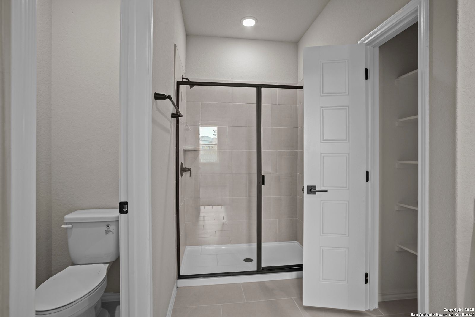 Elegant master bathroom with black-framed glass shower, toilet, and open closet in Davidson Homes The Douglas F, San Antonio