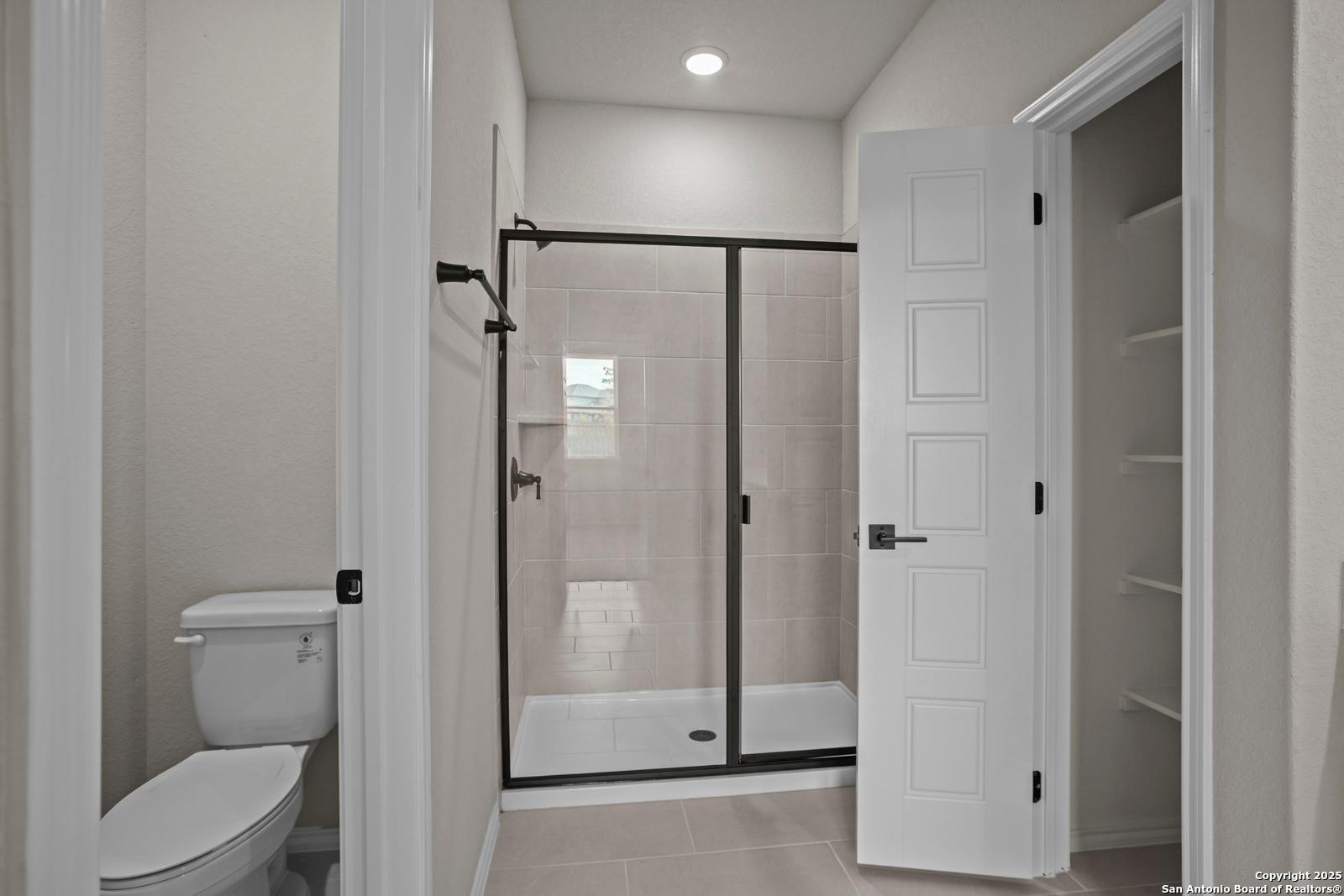 Elegant master bathroom with black-framed glass shower, toilet, and open closet in Davidson Homes The Douglas F, San Antonio