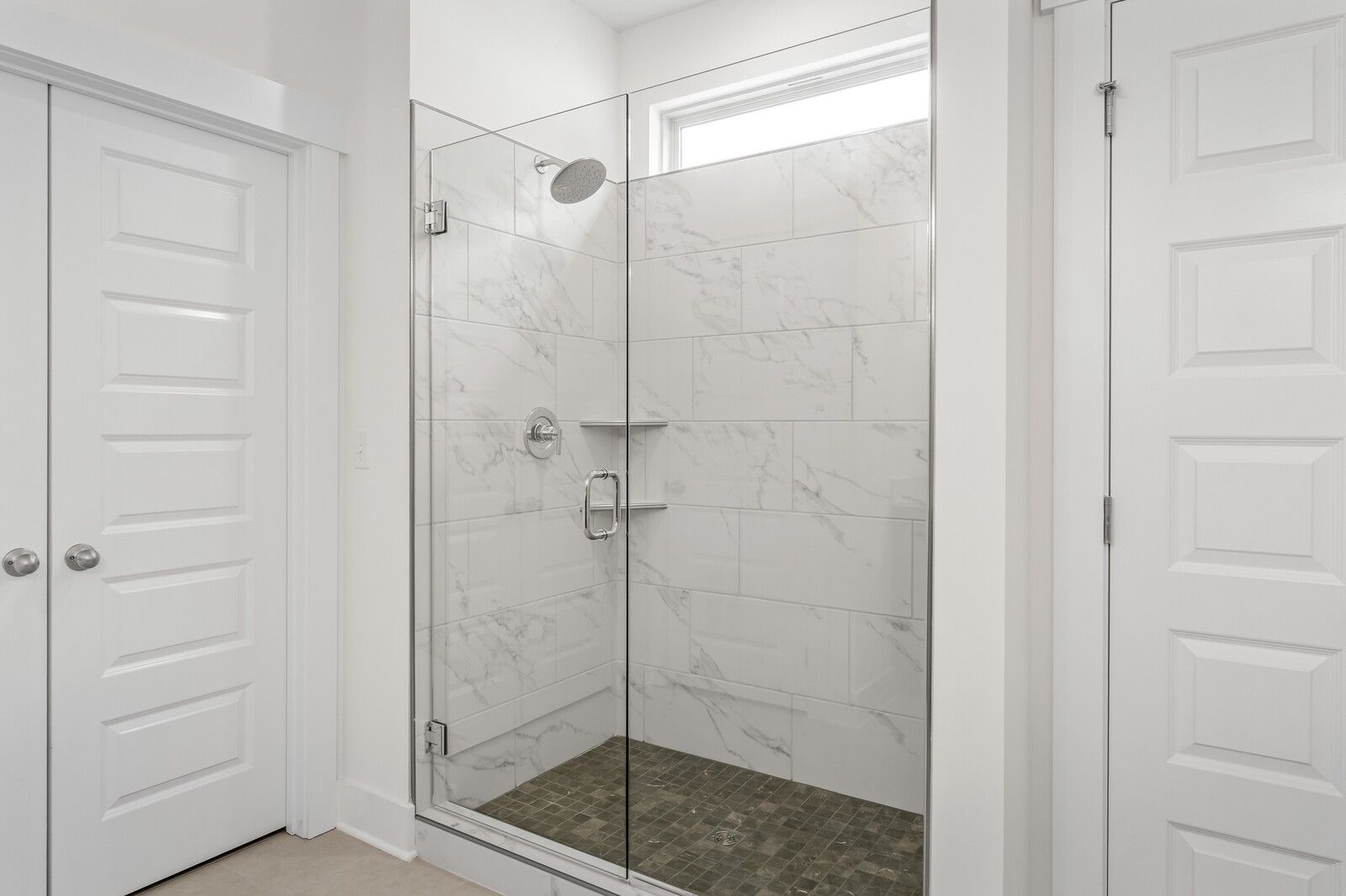 Walk-in shower with marble-look tile, glass door, and stone floor in The Ridgeport C home at Woods Crossing, Gallatin, TN.