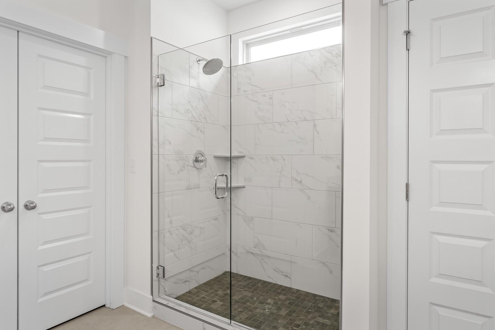 Walk-in shower with marble-look tile, glass door, and stone floor in The Ridgeport C home at Woods Crossing, Gallatin, TN.