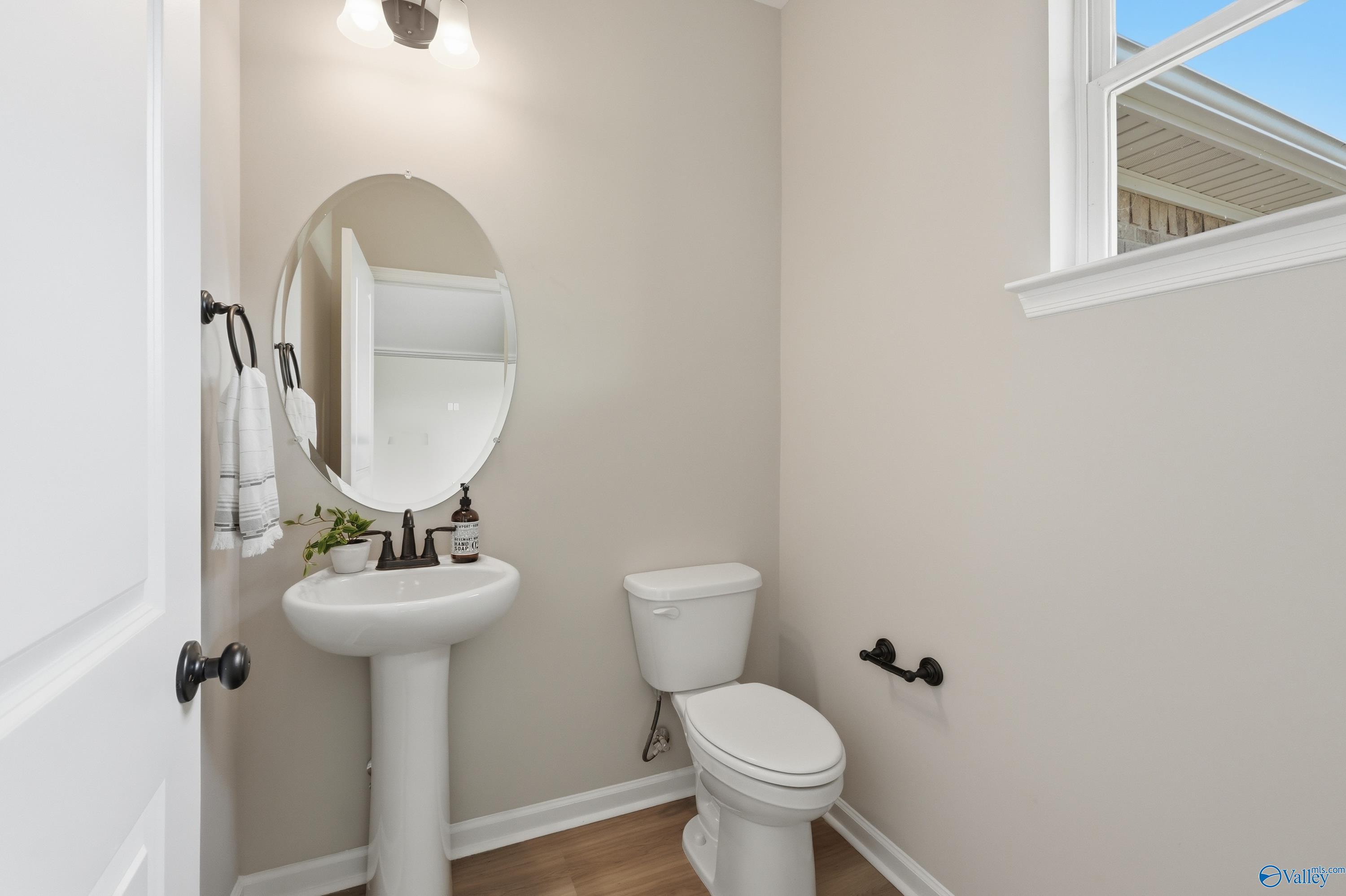Elegant powder room featuring pedestal sink, round mirror, white toilet, and beige walls in Davidson Homes The Dorado, Huntsville