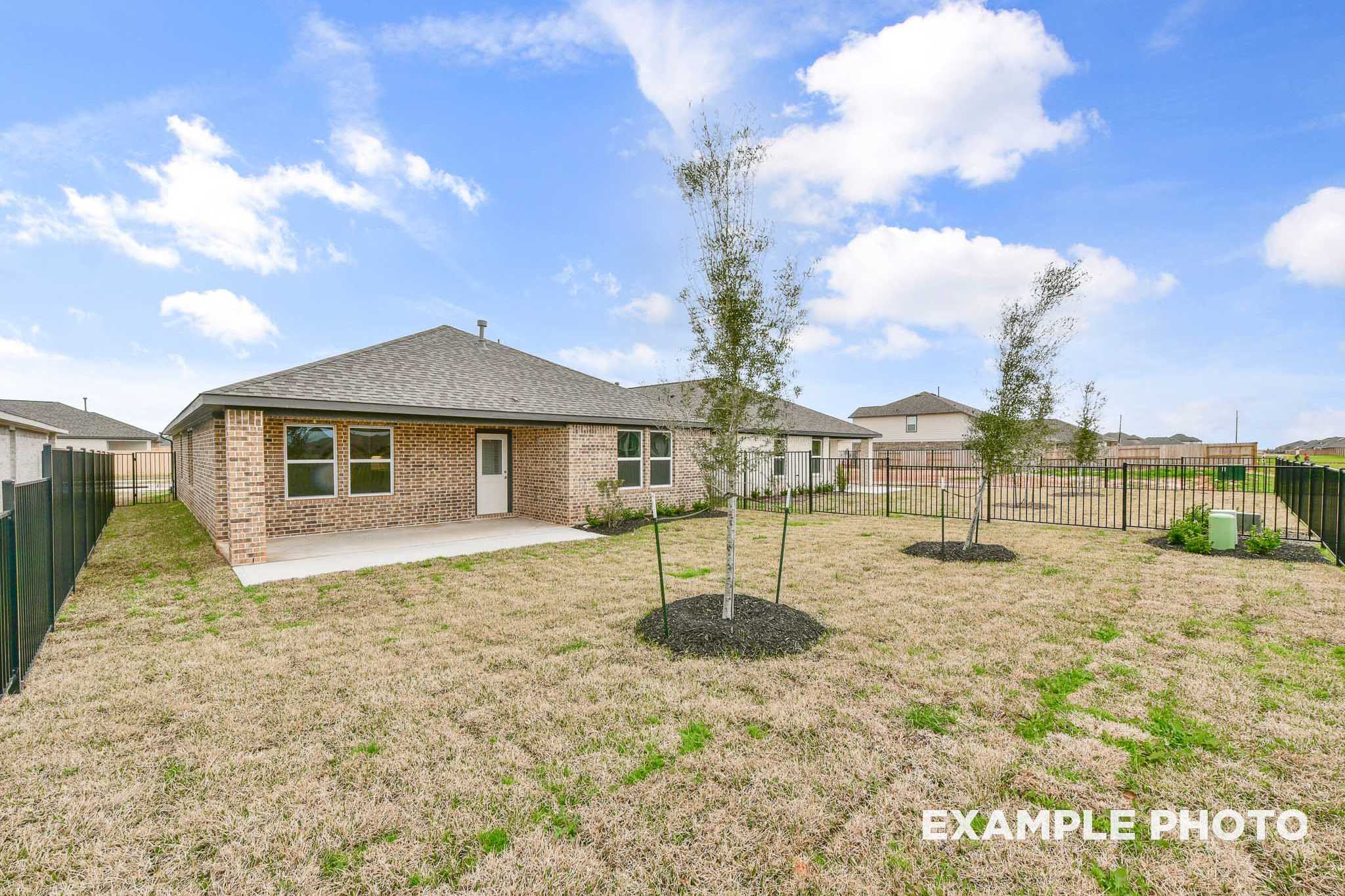 Backyard view of The Laguna A single-story home with covered patio, brick exterior, fenced yard, young trees, and lush grass in Rosharon Texas
