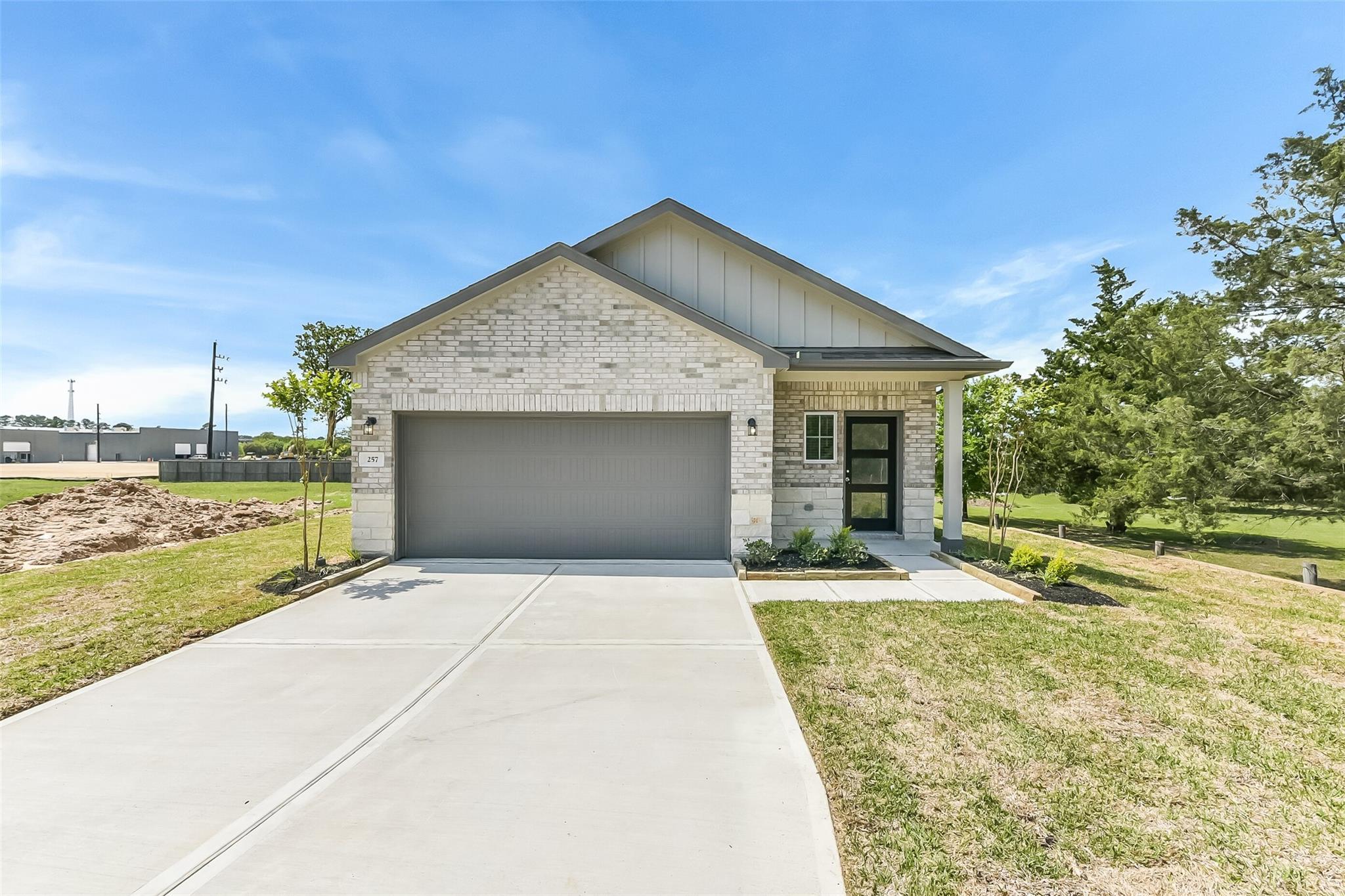 White brick single-story 3-bedroom home with 2-car garage, driveway, front porch, trees, and blue sky in Windmill Estates, Magnolia, Texas - Davidson Homes The Frio G