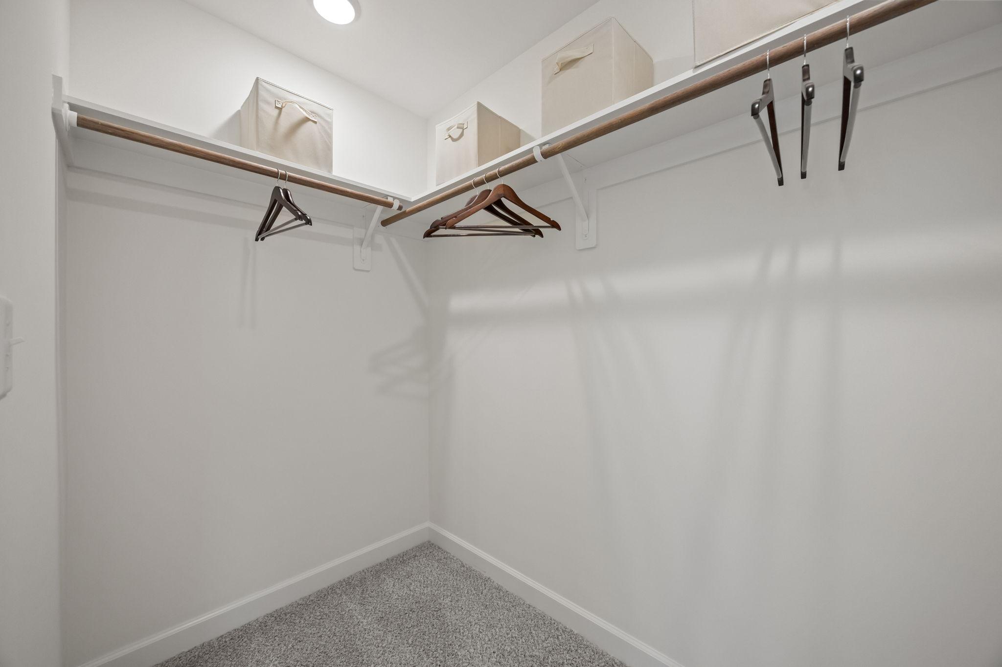 Spacious walk-in closet in The Mitchell master suite featuring wood shelving, hanging rods, and neutral carpeting.