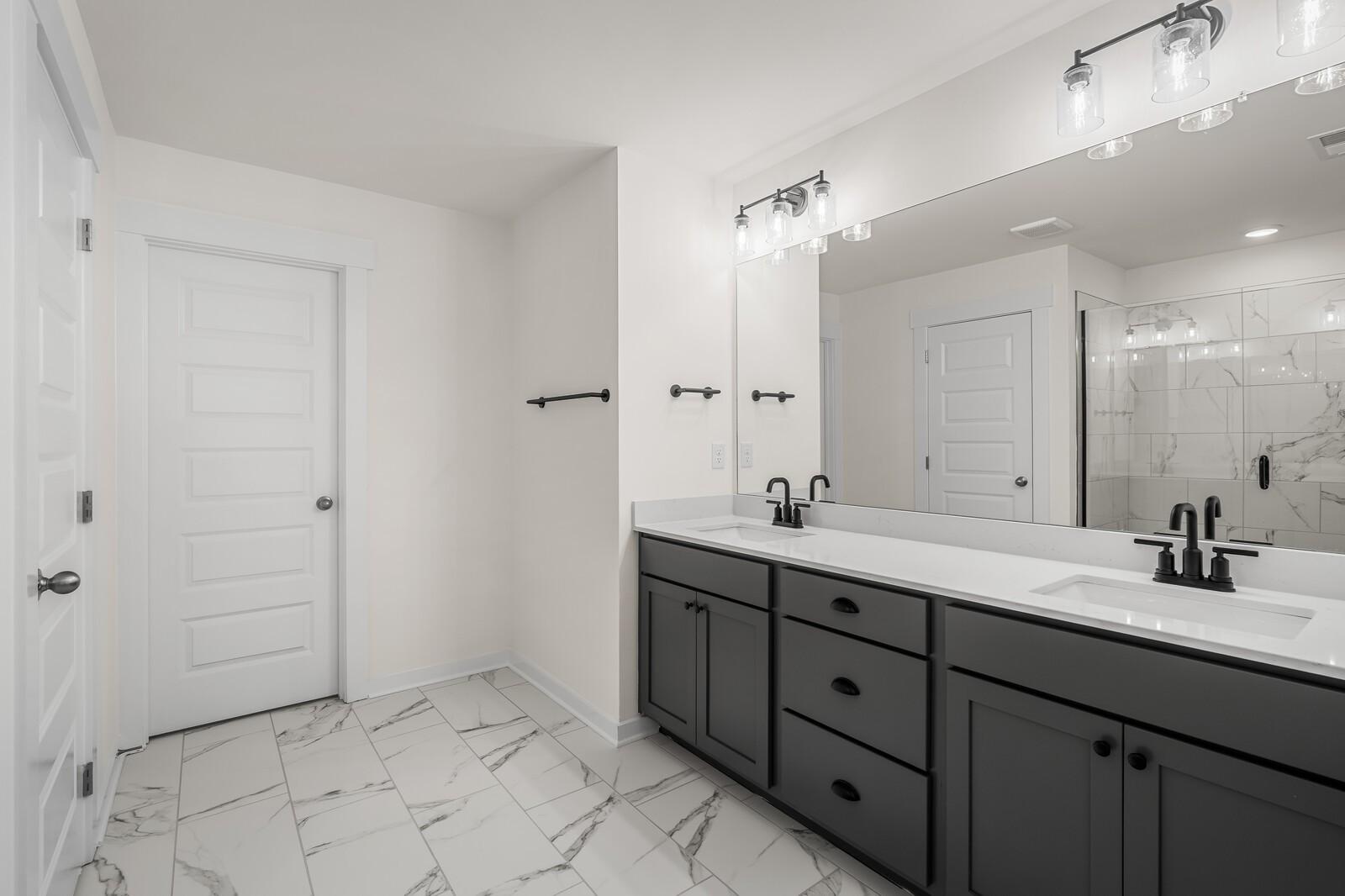 Modern bathroom with double vanity, dark cabinets, and marble tile flooring in The Willow home at Woods Crossing, Gallatin.