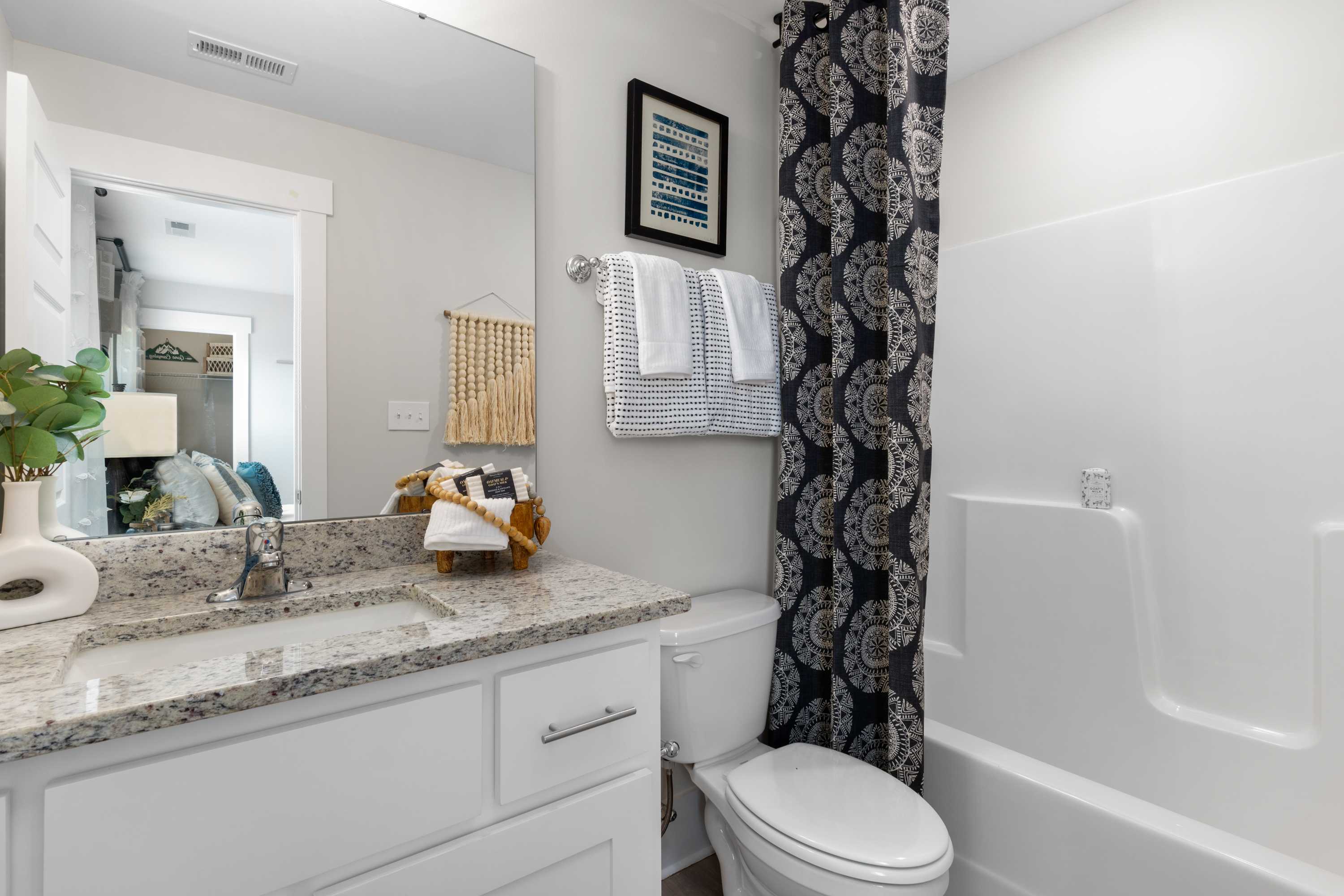 Spacious master bathroom in The Chelsea B featuring white vanity, granite countertop, walk-in shower, and blue patterned curtain