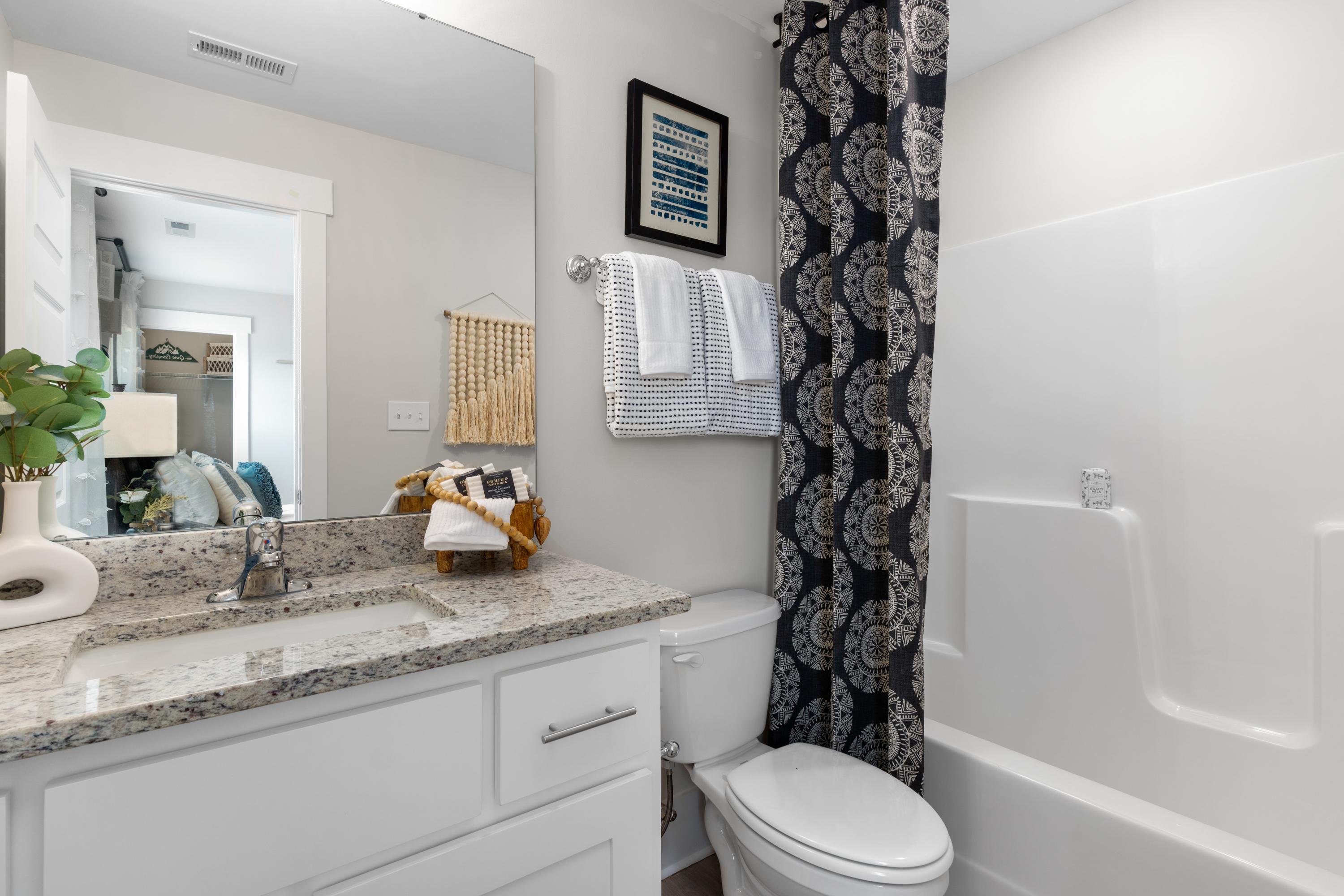 Spacious master bathroom in The Chelsea A with quartz vanity, large mirror, potted plant, and blue patterned shower curtain