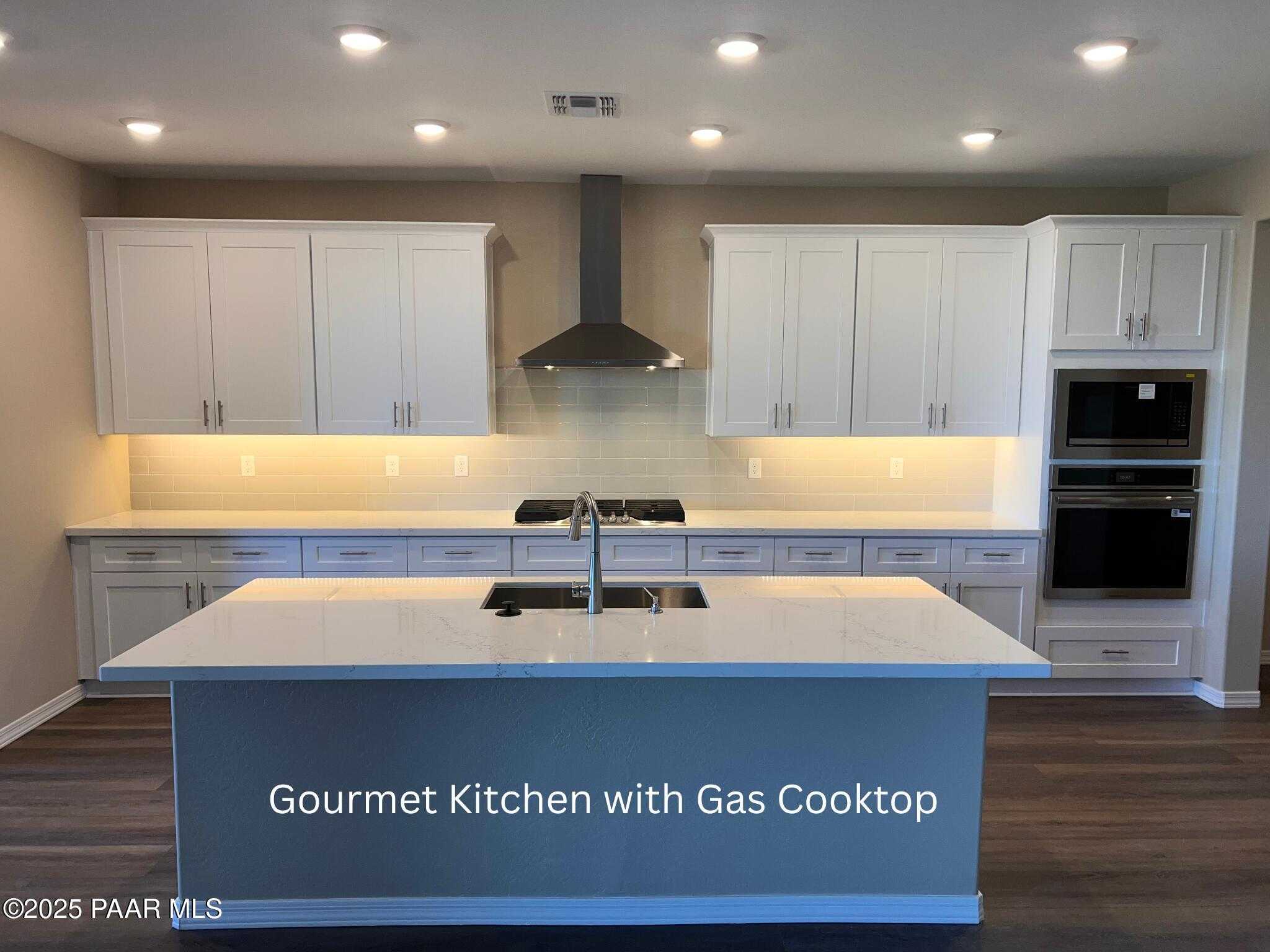Gourmet kitchen with white shaker cabinets, gray quartz island, gas cooktop, and double ovens in Davidson Homes Inspiration A, Prescott Valley, AZ