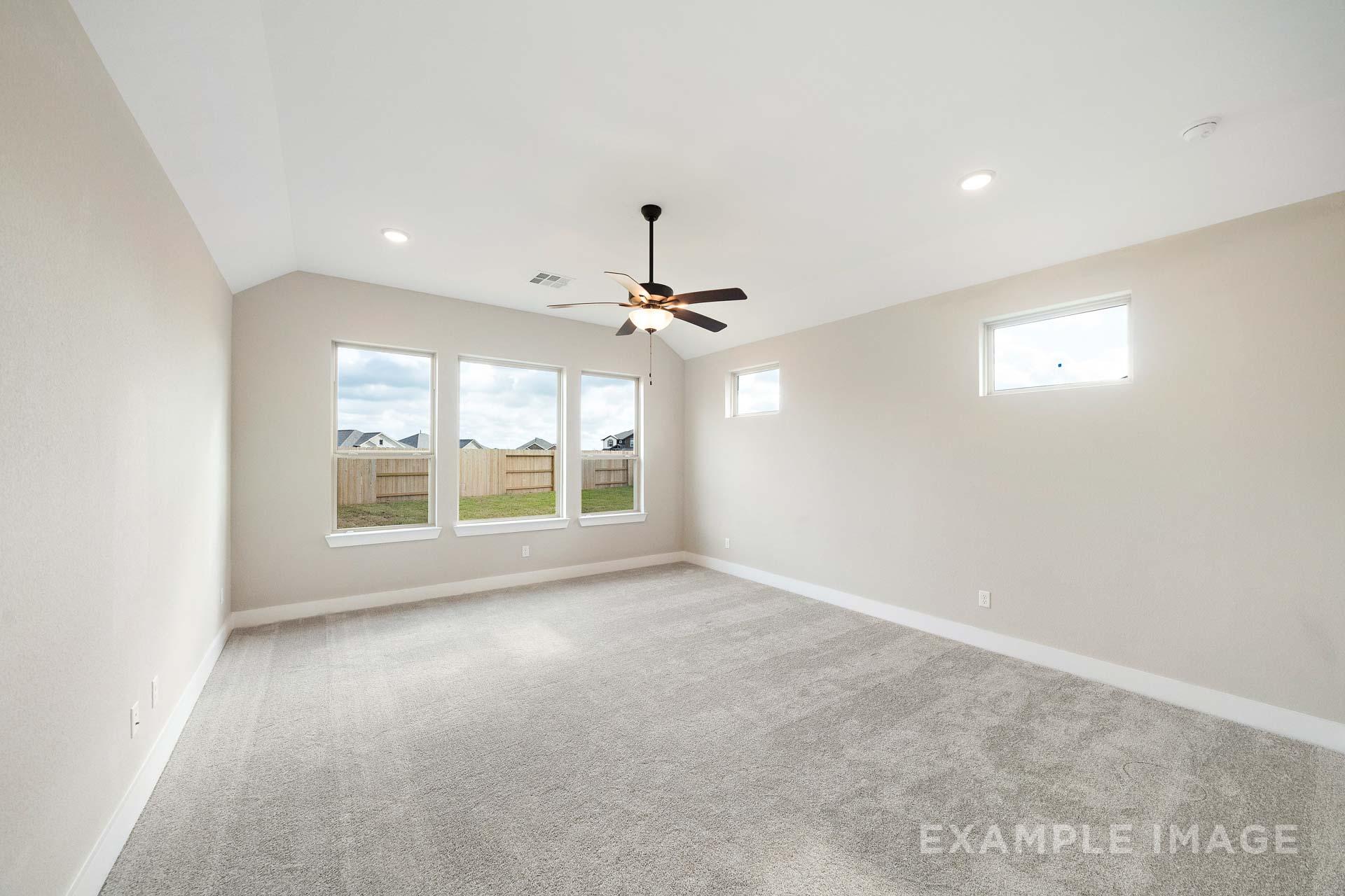 Spacious master bedroom in The Elizabeth A featuring large windows, ceiling fan, neutral beige walls, and plush carpet