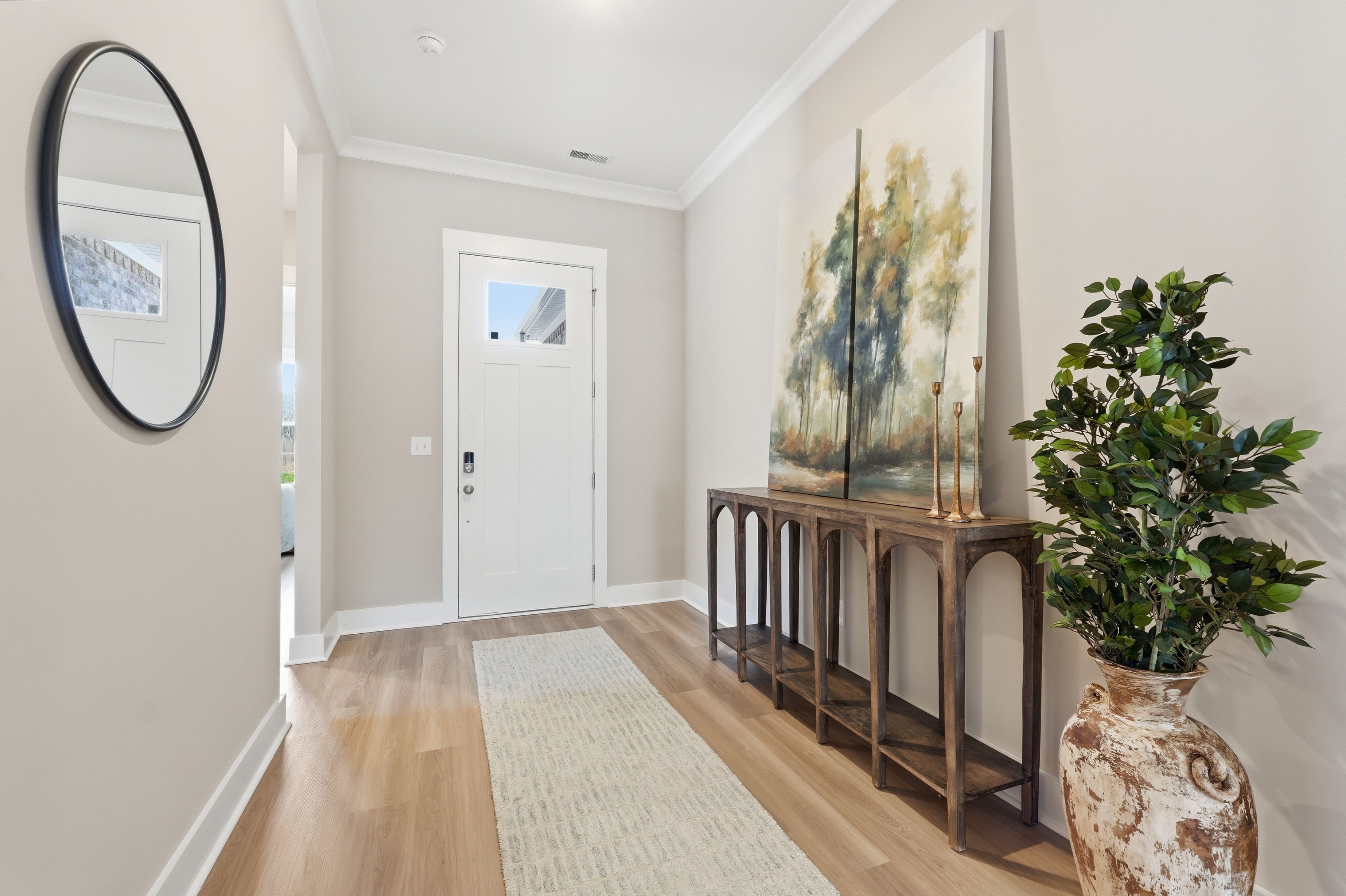 Elegant entryway hallway at The Meadows at Hampton Cove in Owens Cross Roads AL with wood floors beige walls round mirror and console table art