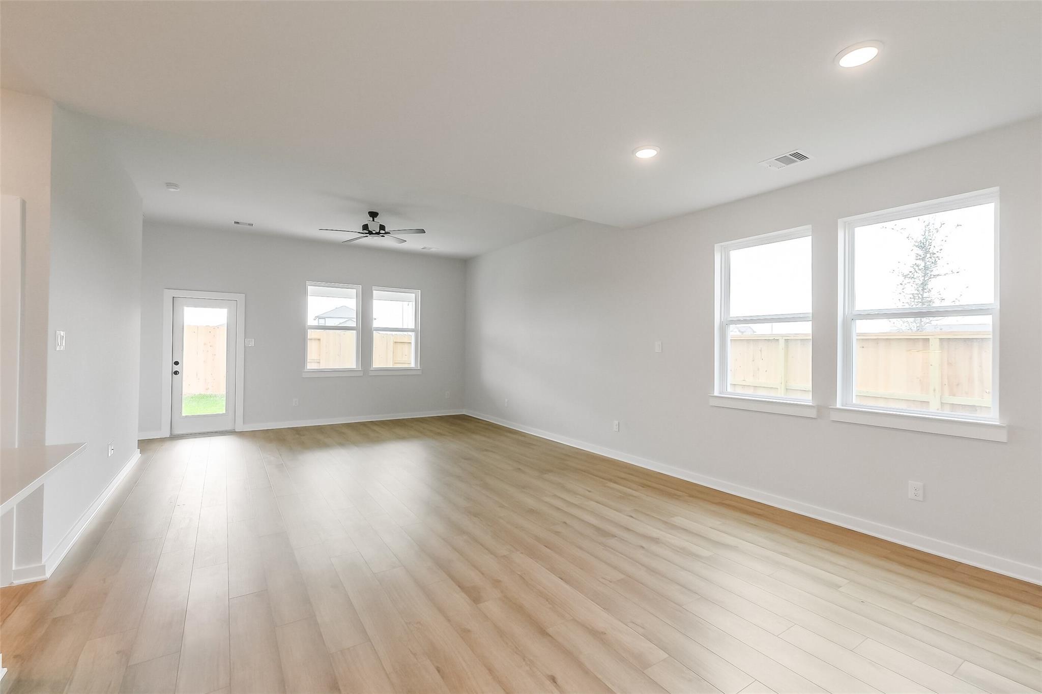 Bright empty living room with light hardwood floors, large windows, ceiling fan in Davidson Homes Tierra B, Beasley, Texas