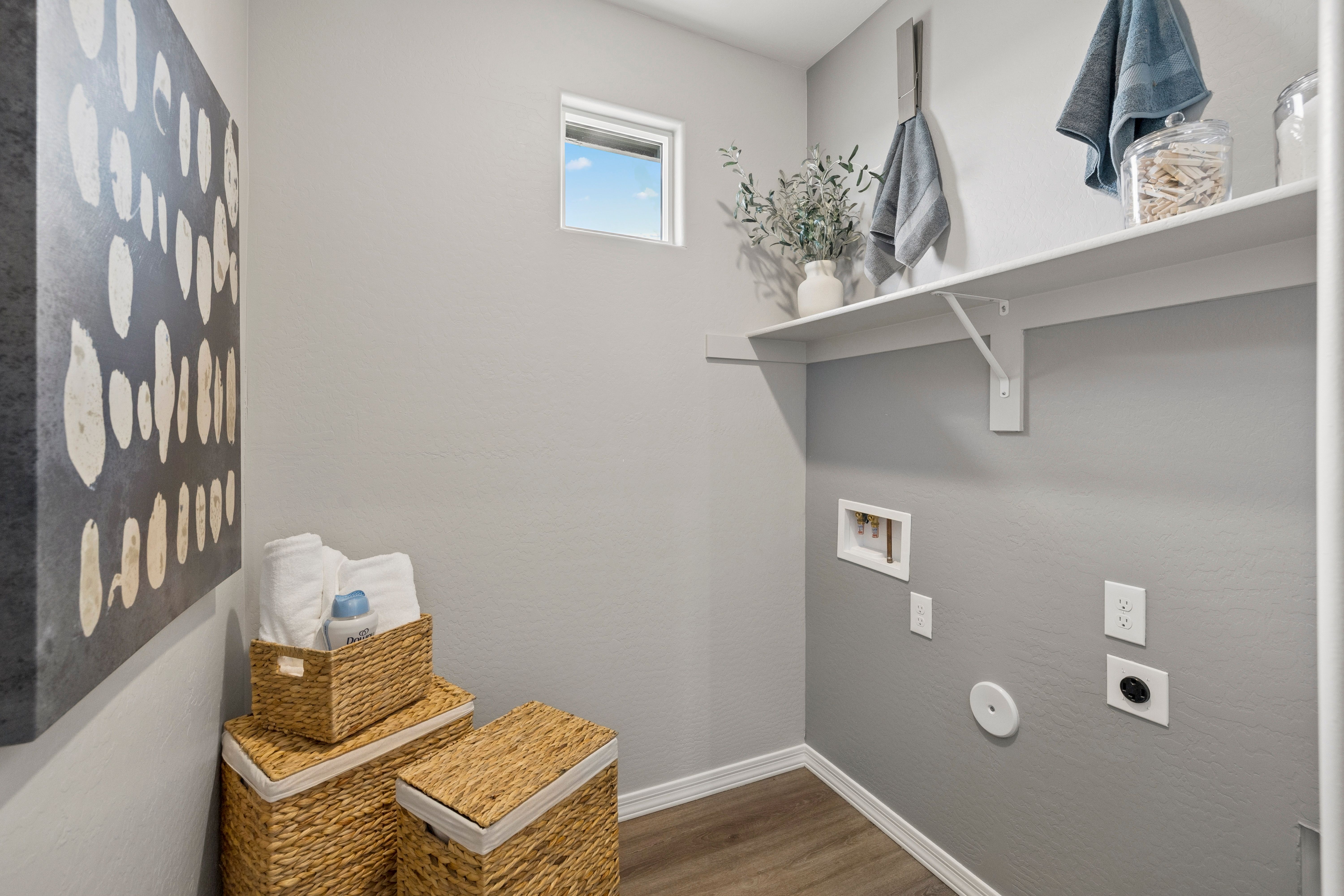 Spacious laundry room at South Ranch in Prescott AZ with gray walls, utility sink, wicker baskets, towels and floating shelves