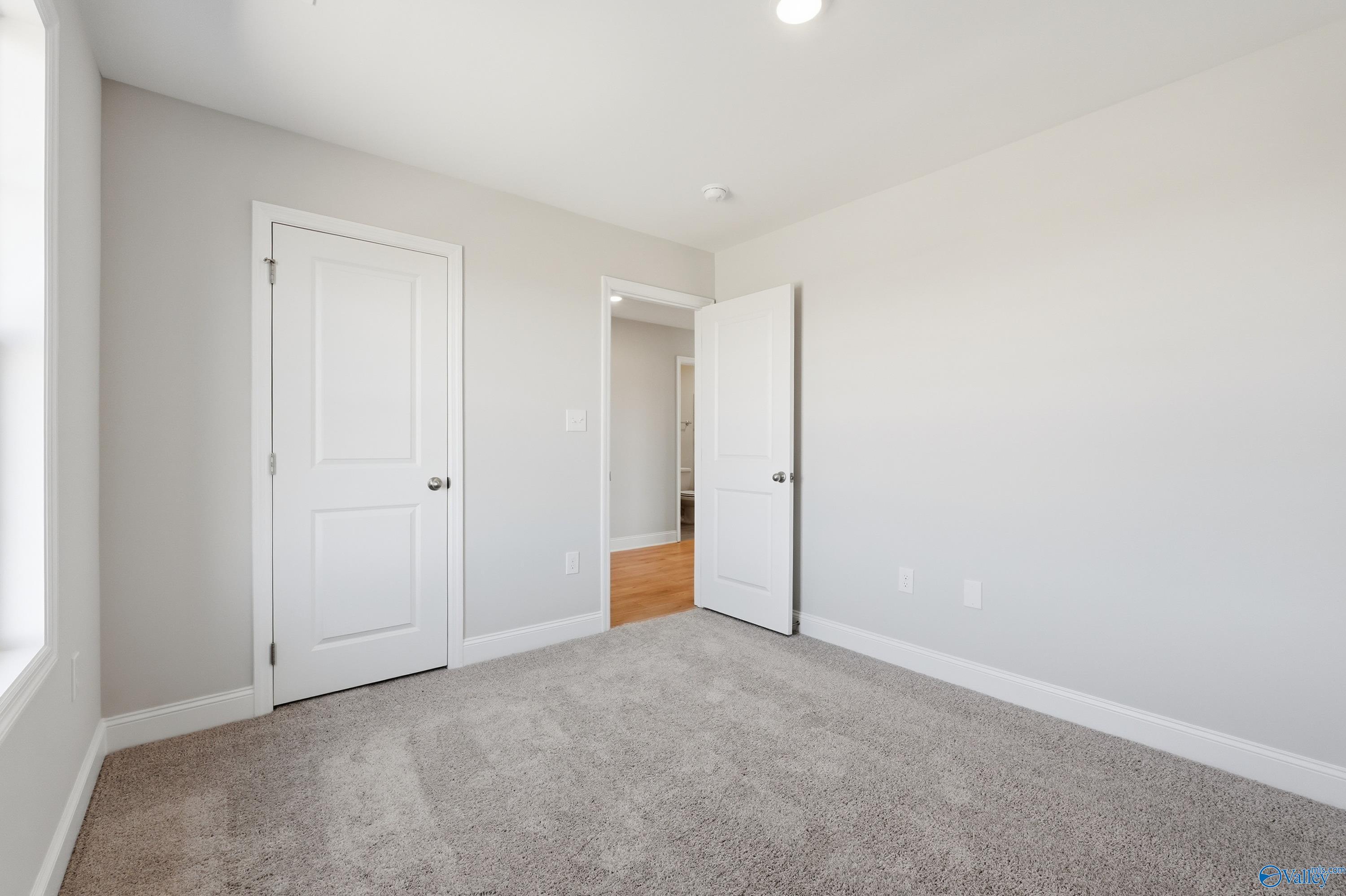 Secondary bedroom featuring gray carpet and walls, open door to bathroom in Davidson Homes The Butler, New Market, Alabama
