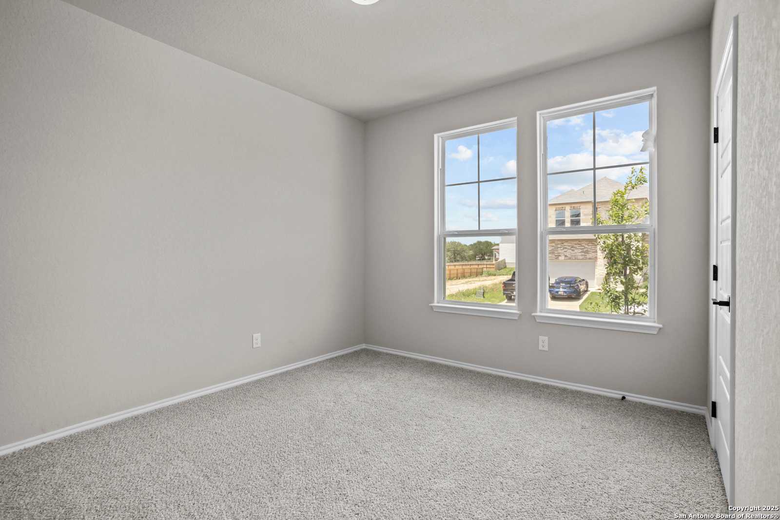 Bright secondary bedroom with light gray walls, carpet floor, and large windows overlooking backyard in Davidson Homes The Daphne G, San Antonio