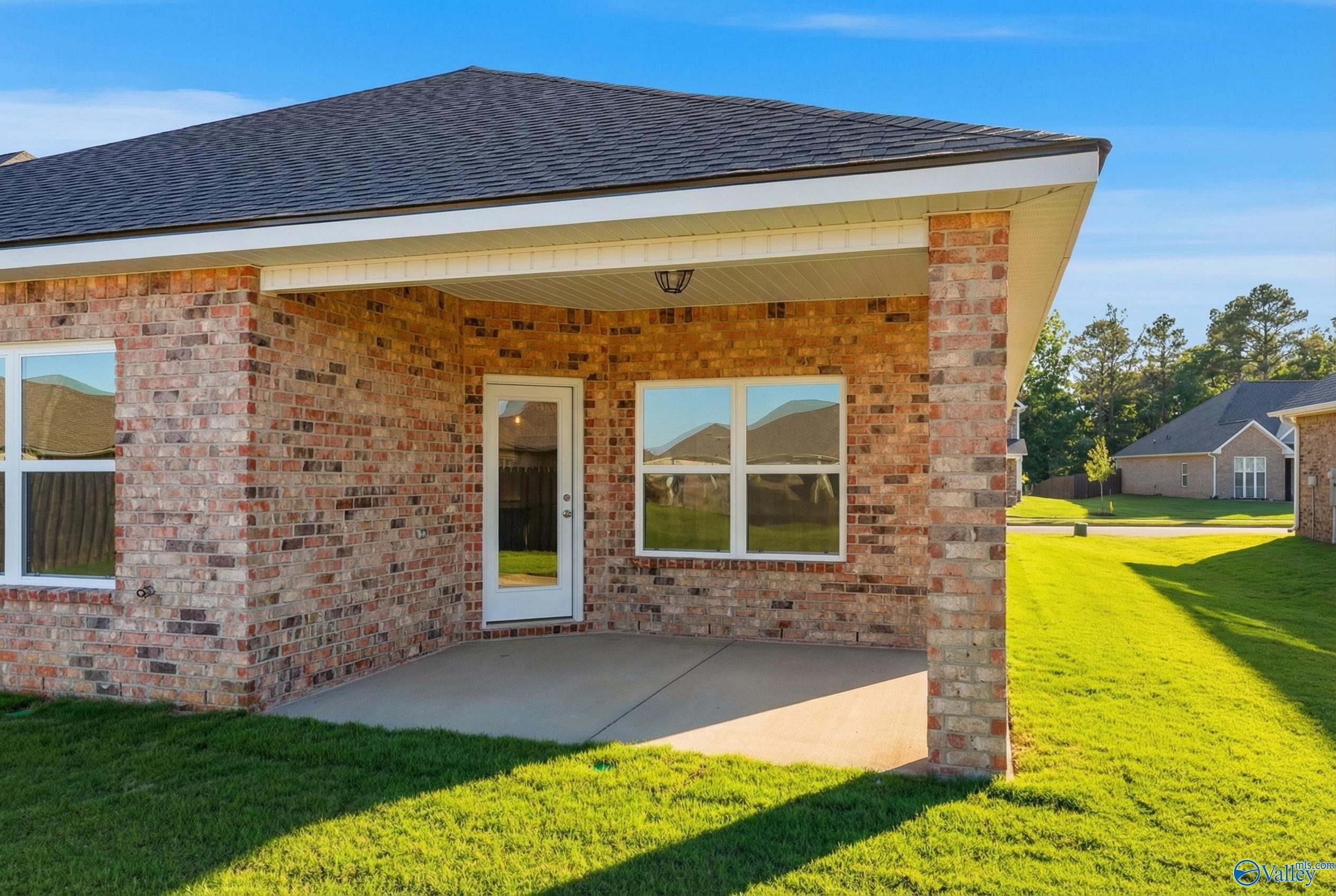 Brick home exterior with covered porch, glass entry door, and lush green lawn in Creekside, Harvest, Alabama