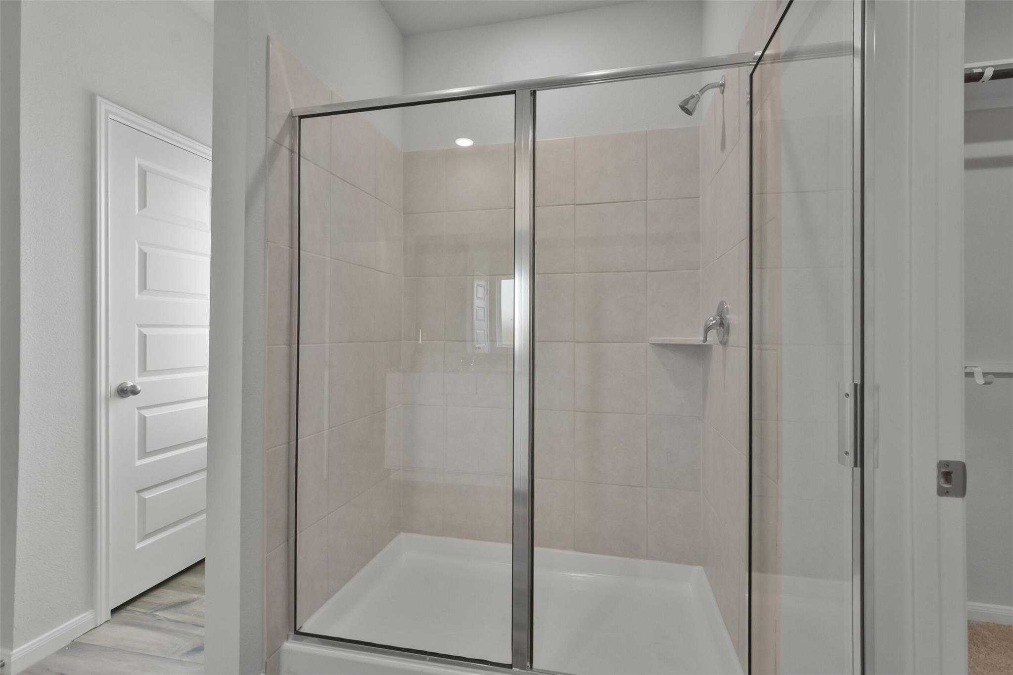 Modern walk-in shower with beige tile walls and glass door in master bathroom of Davidson Homes Tierra A, Dayton, Texas