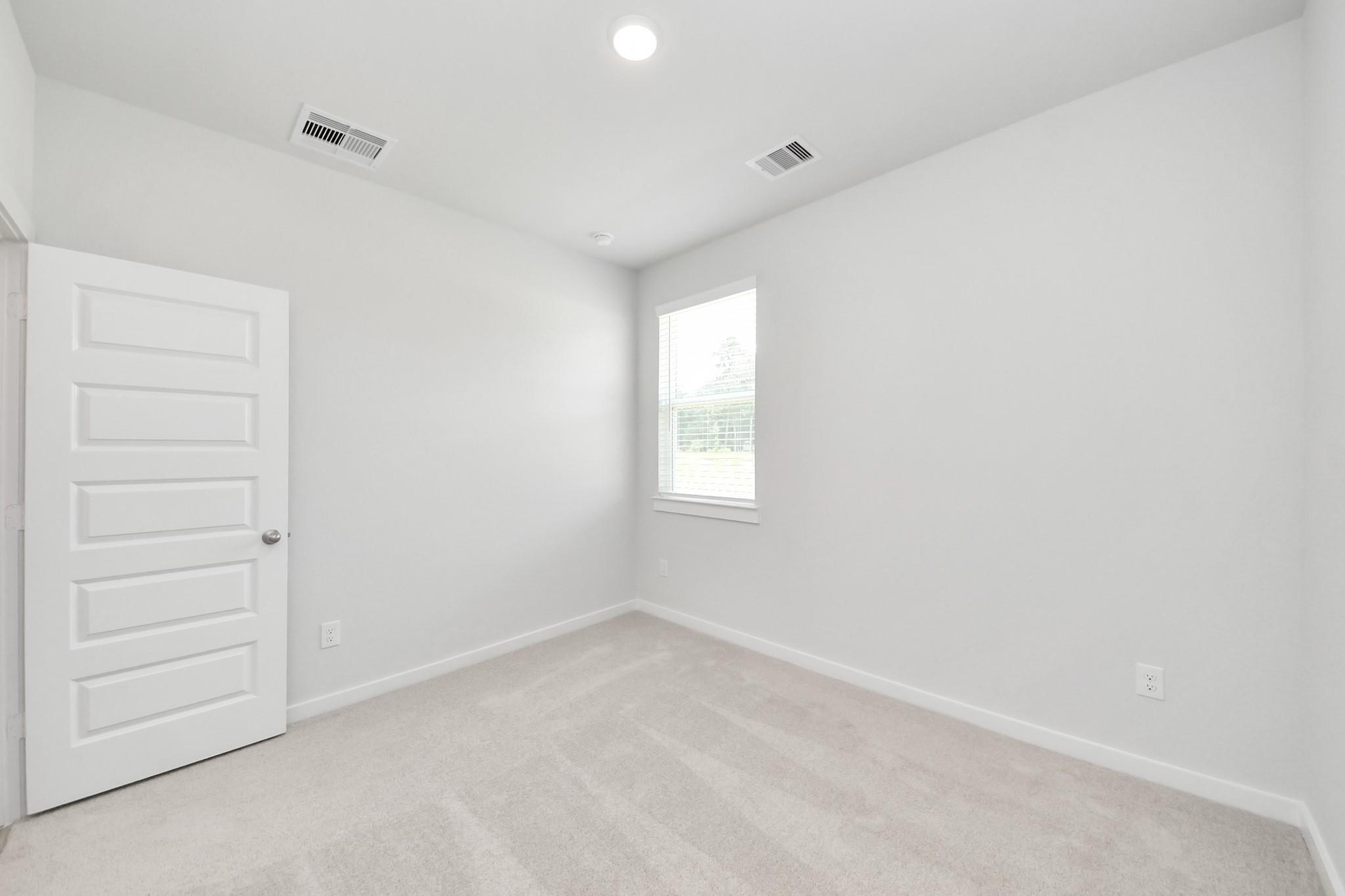 Bright, spacious secondary bedroom with neutral carpet in The Frio F floor plan at Liberty Estates, Cleveland, Texas.