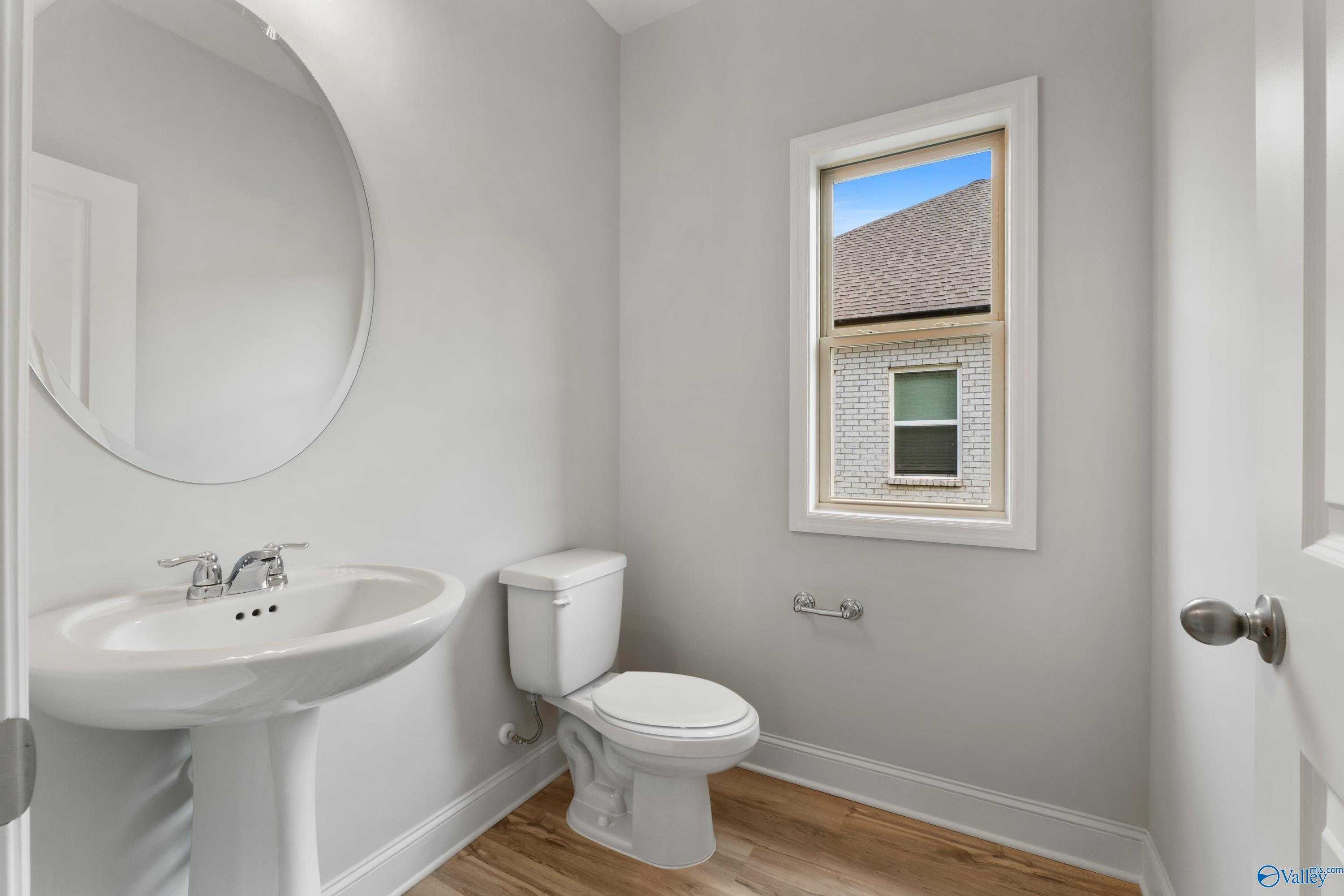Elegant powder room with pedestal sink, round mirror, and window in Davidson Homes The Chelsea C, Harvest, Alabama