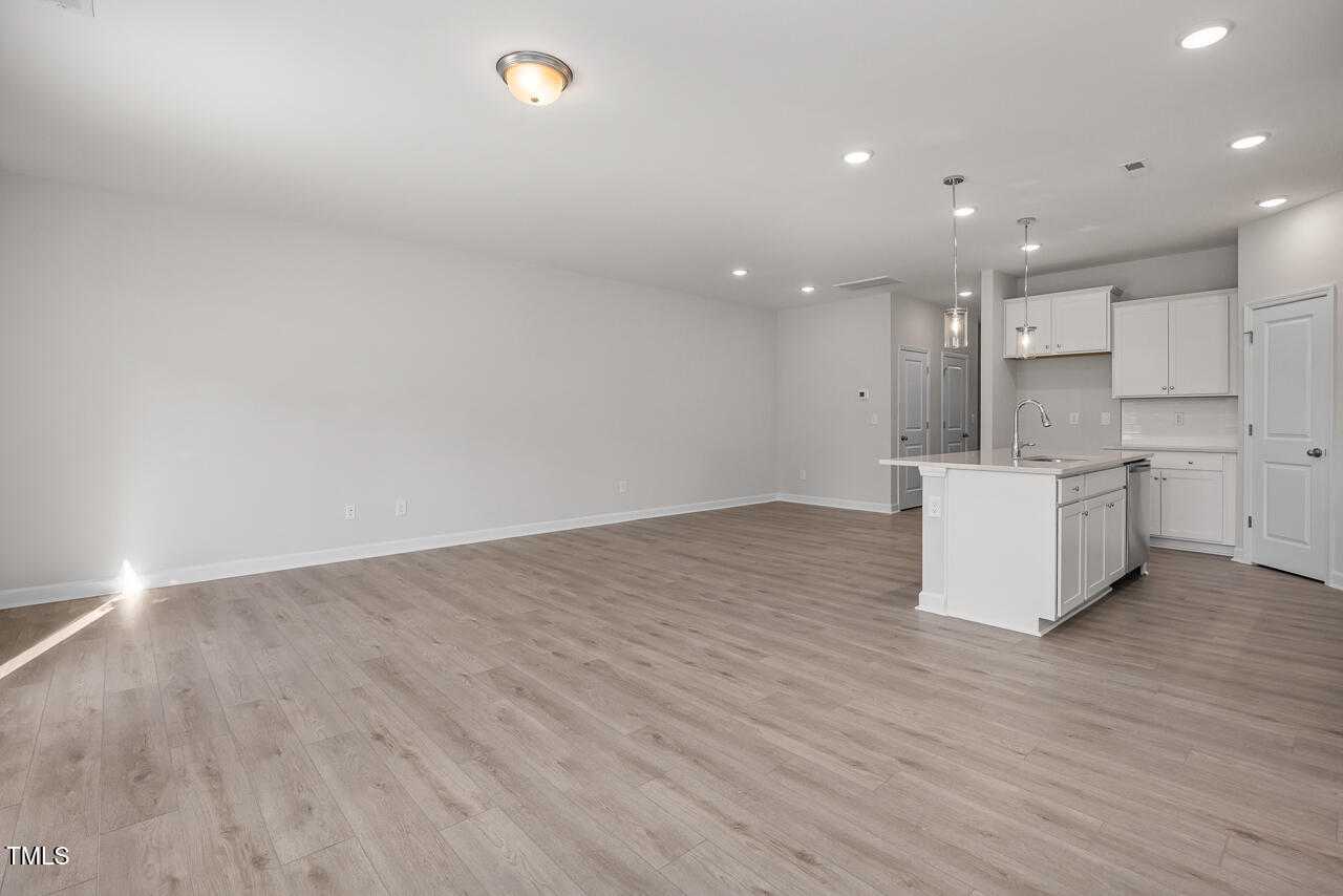 Open-concept living space with white kitchen island, cabinets, hardwood floors, and recessed lighting in The Warren Interior, Fuquay-Varina, NC