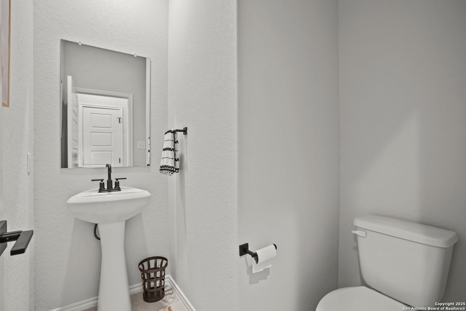 Elegant powder room with white pedestal sink, frameless mirror, and toilet in Davidson Homes The Douglas C, Seguin, Texas