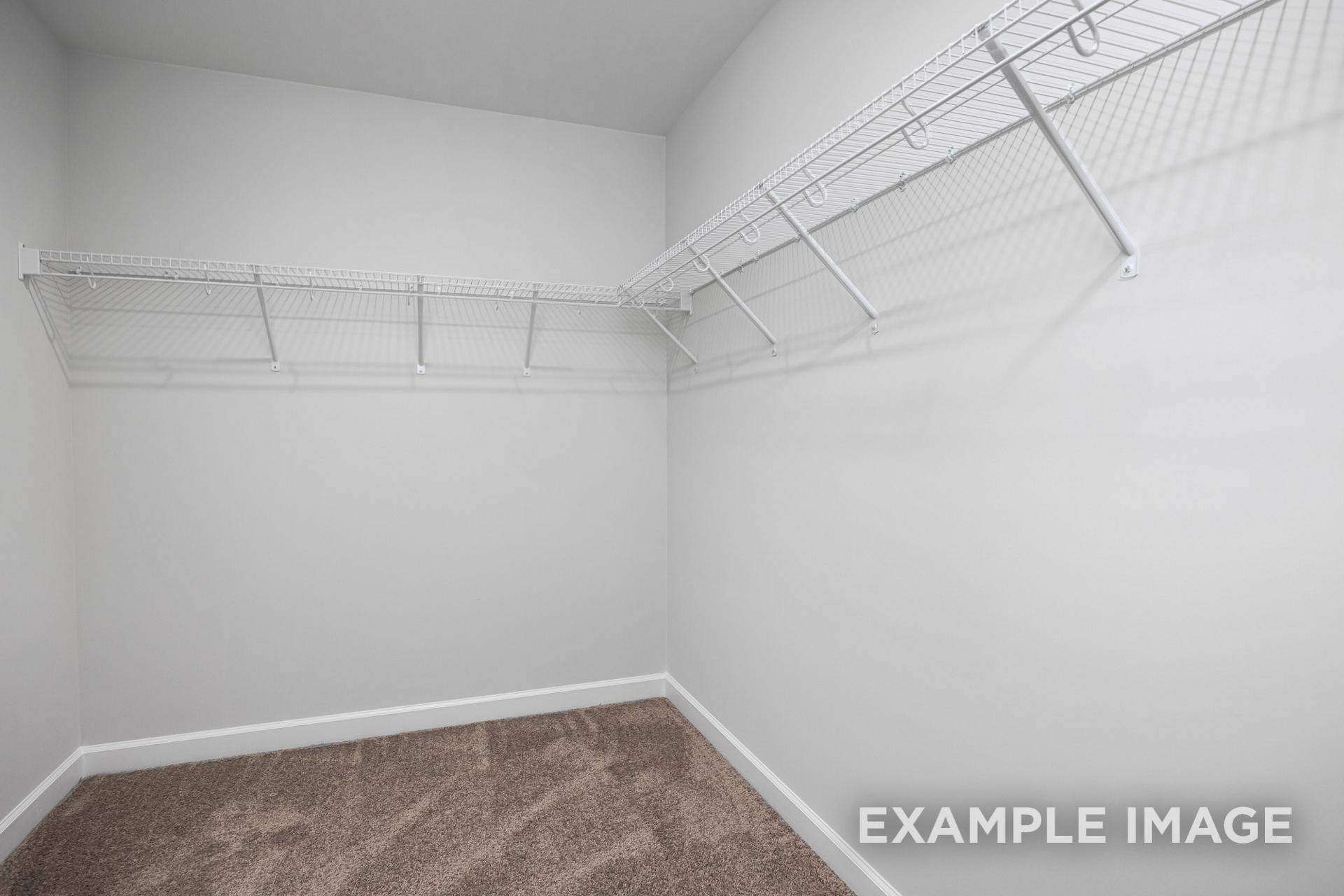 Spacious walk-in closet in The Gavin B master suite featuring white wire shelving along walls and beige carpet flooring
