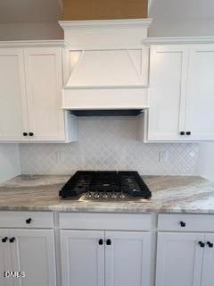 White kitchen with gas cooktop, custom hood, and stone countertops in The Ash C floor plan at Woodland Crossing, Zebulon.