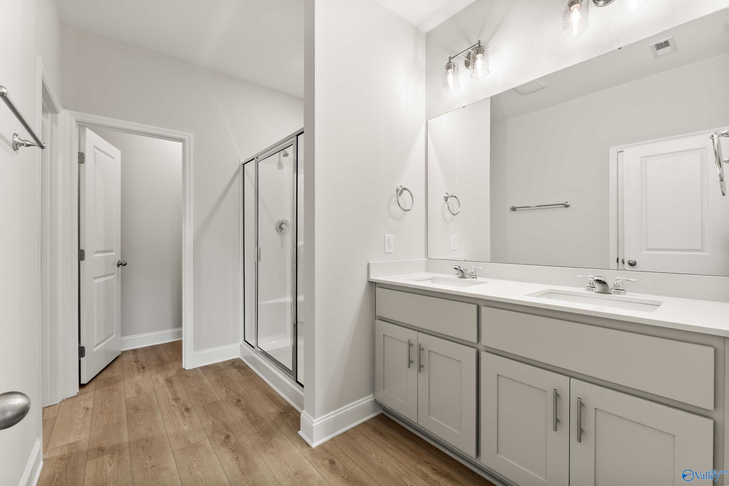 Modern master bathroom featuring double vanity, frameless glass shower, and hardwood floors in Davidson Homes The Daphne C, Athens, Alabama