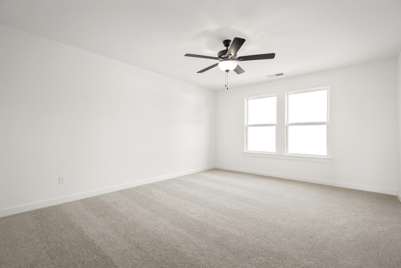 Bright empty bedroom with white walls, double windows, ceiling fan, and beige carpet in Davidson Homes The Logan C, Gallatin, TN