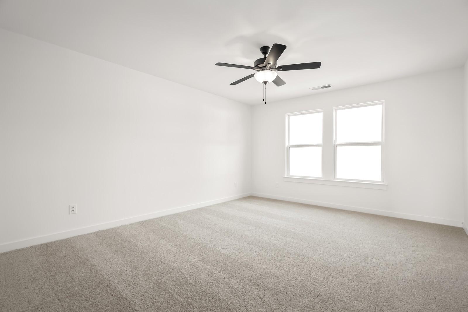 Bright empty bedroom with white walls, double windows, ceiling fan, and beige carpet in Davidson Homes The Logan C, Gallatin, TN