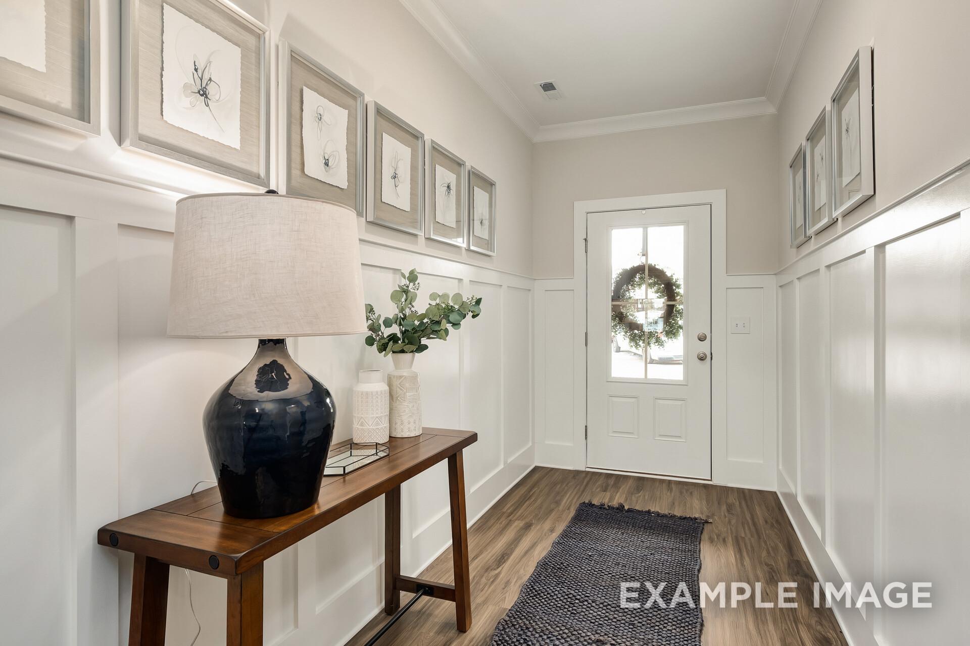 Spacious entryway in The Daphne D with white paneled walls, console table, blue lamp, eucalyptus decor, and wreath-adorned door