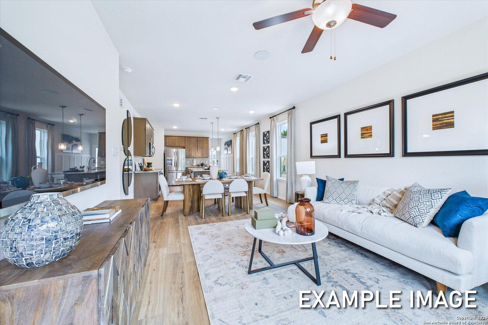 Spacious open-concept living room with white sofa, wooden dining table, and kitchen in Davidson Homes The Gillian C, San Antonio