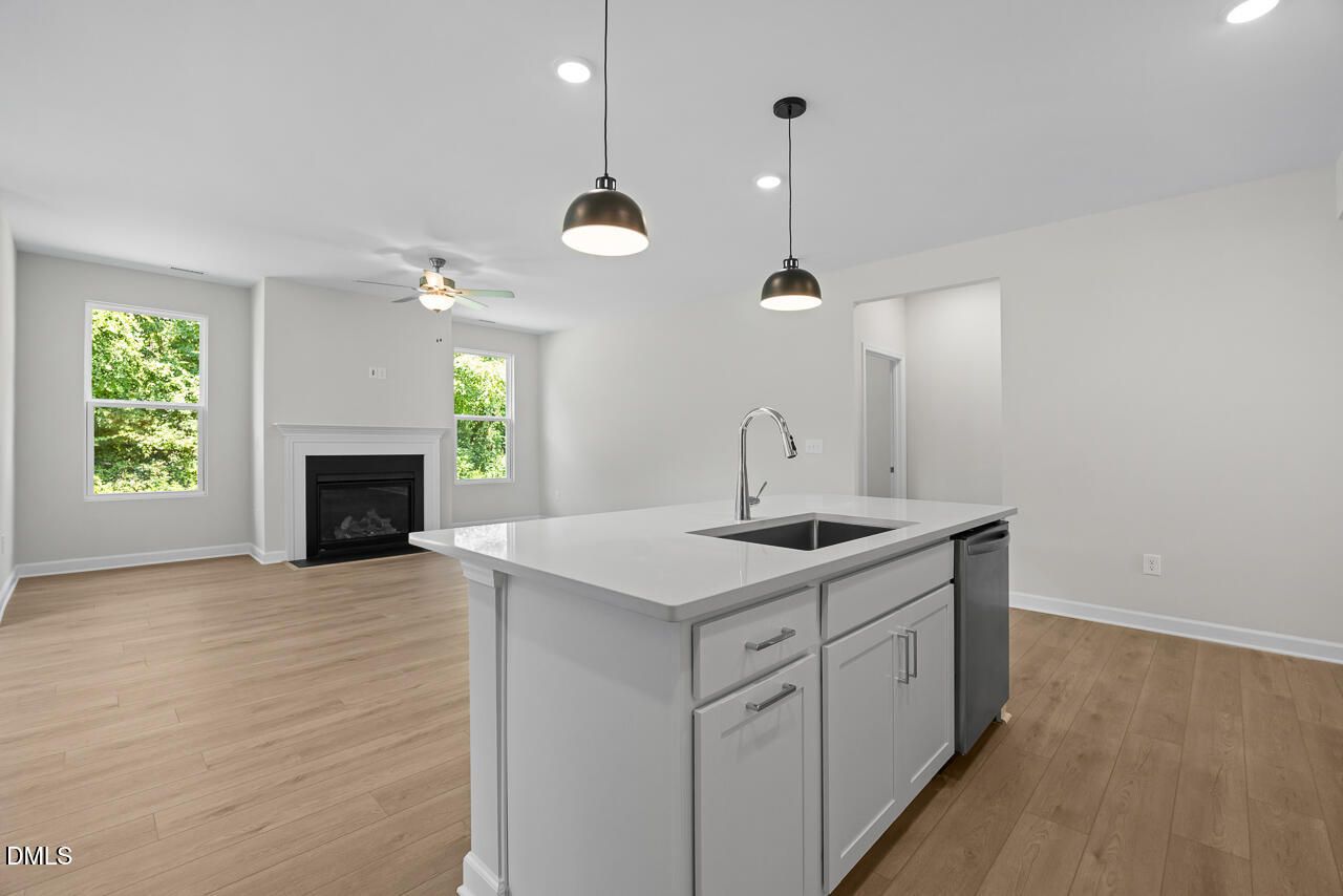 Open-concept kitchen island with sink and white cabinetry beside fireplace in Davidson Homes The Daphne D, Zebulon NC