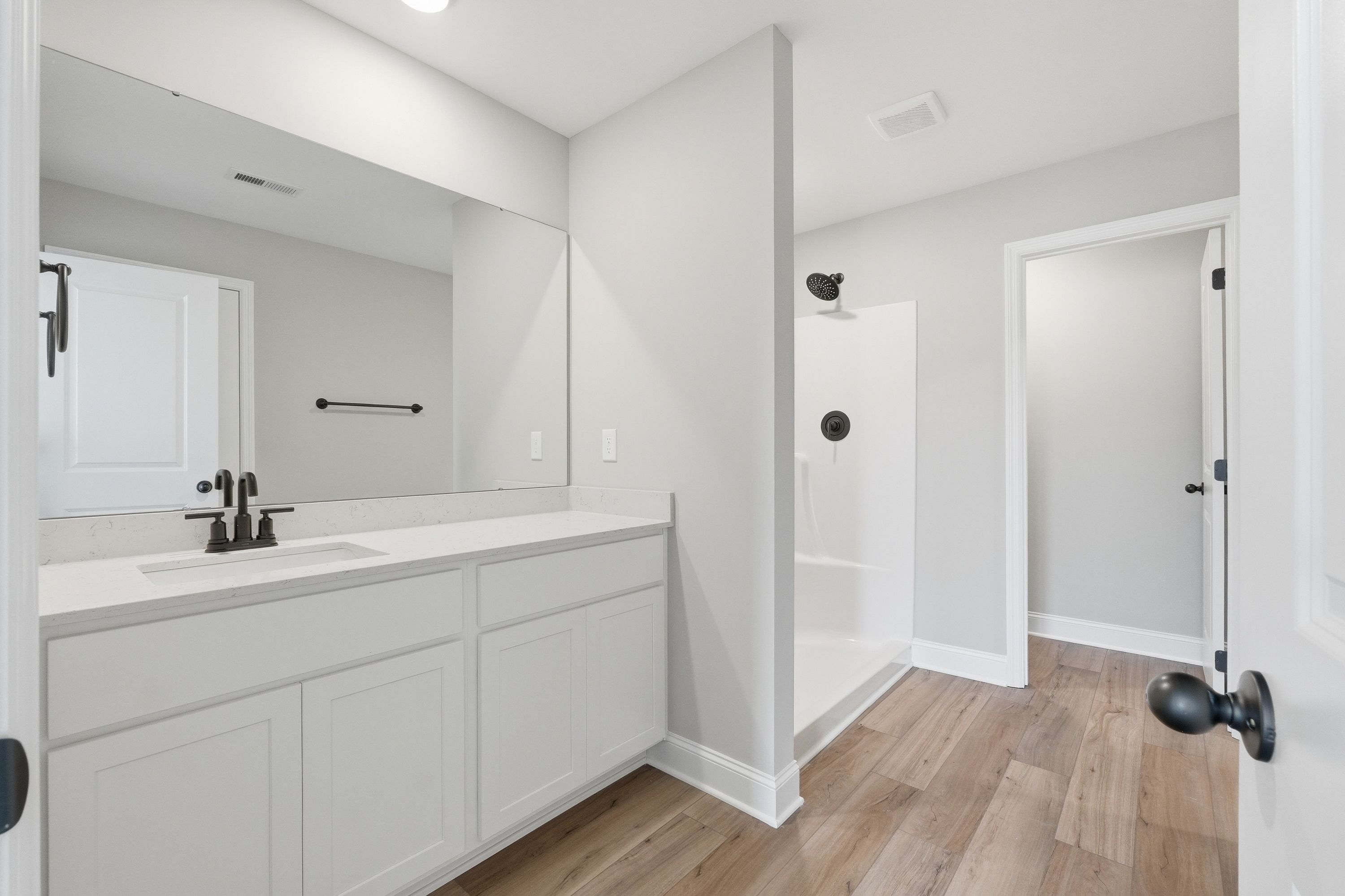 Spacious master bathroom in The Daphne V with white double vanity, large mirror, walk-in shower, and hardwood floors