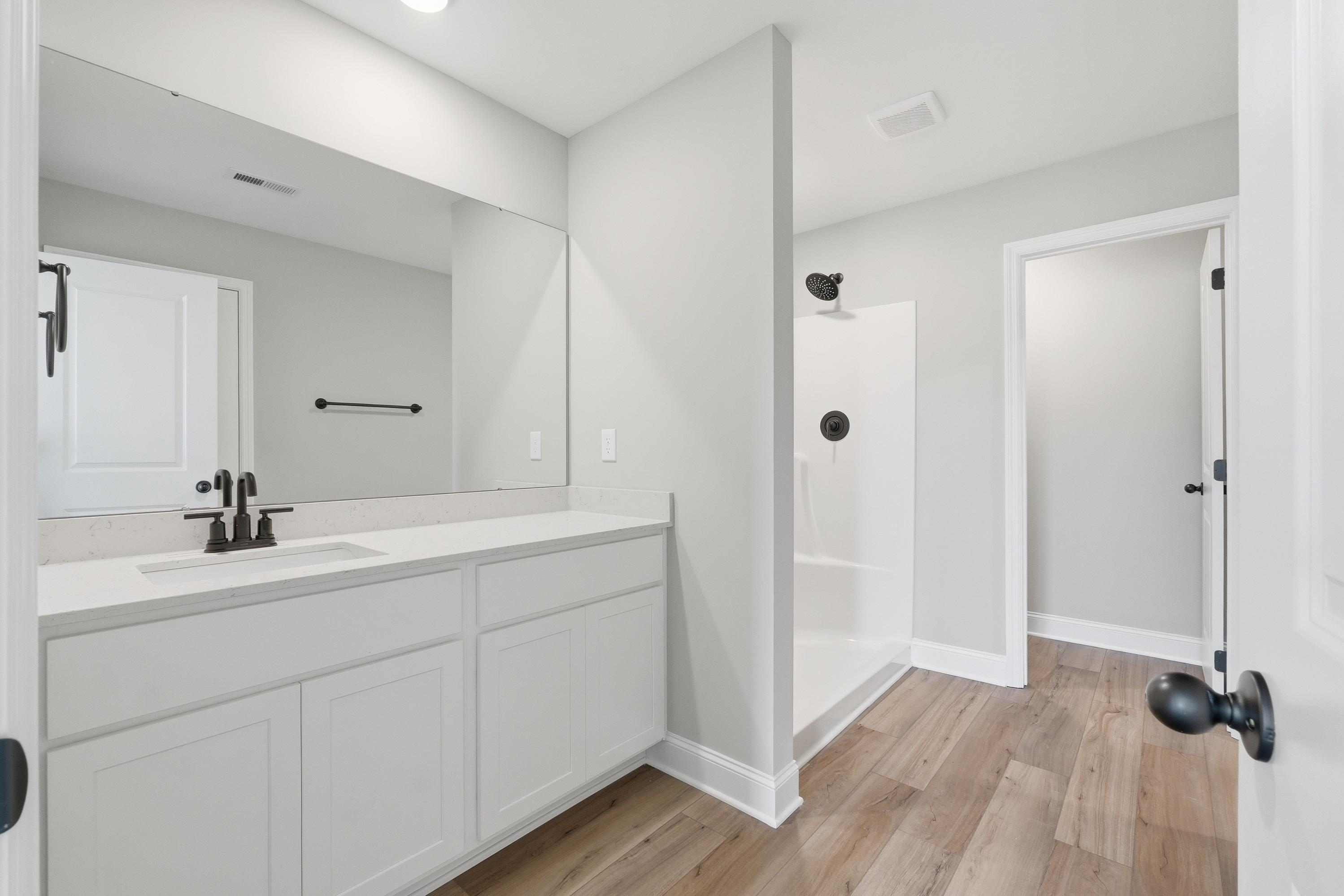 Spacious master bathroom in The Daphne V with white double vanity, large mirror, walk-in shower, and hardwood floors