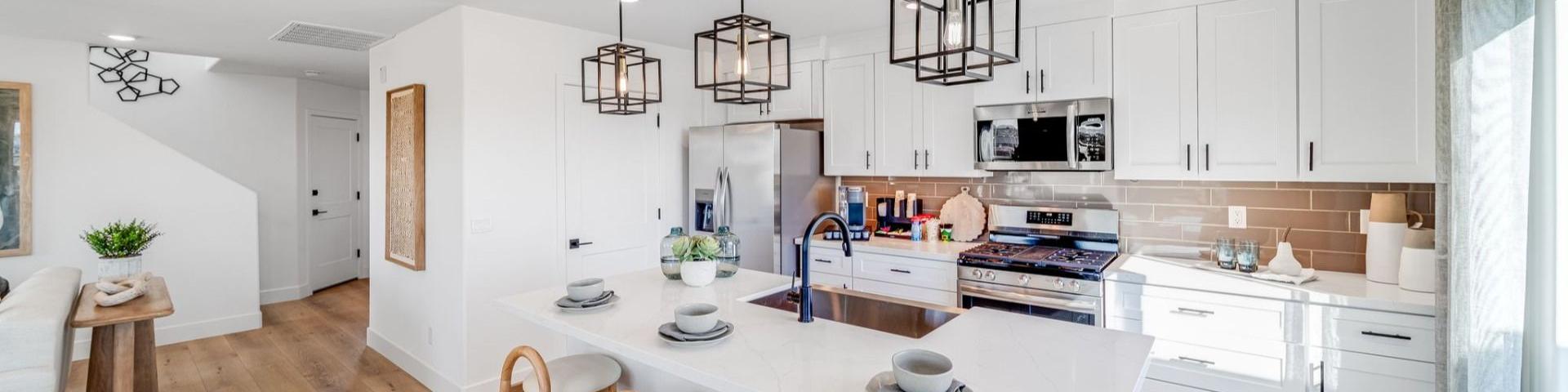 Spacious white kitchen at Senator Cottages in Prescott AZ with quartz island, bar stools, pendant lights, and stainless appliances