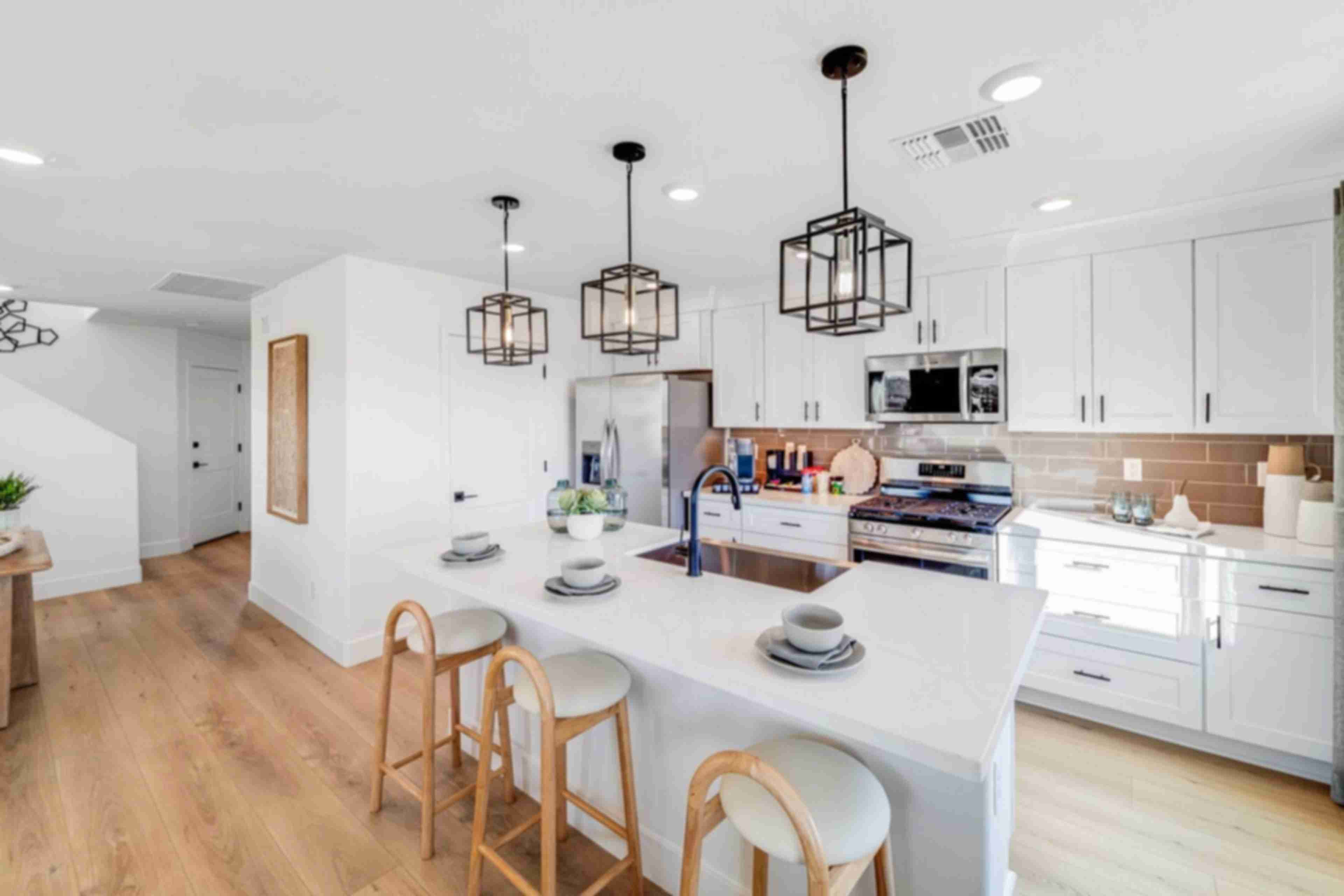 Spacious modern kitchen in Hidden Hills Prescott AZ by Davidson Homes with white cabinets, quartz island, bar stools, and hardwood floors