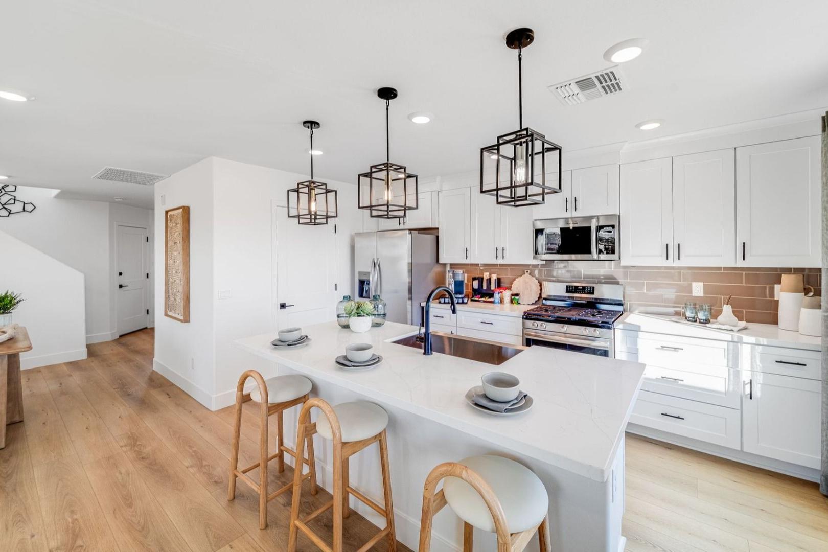 Modern kitchen in Senator Cottages Prescott AZ with white island, bar stools, pendant lights, and hardwood floors by Davidson Homes