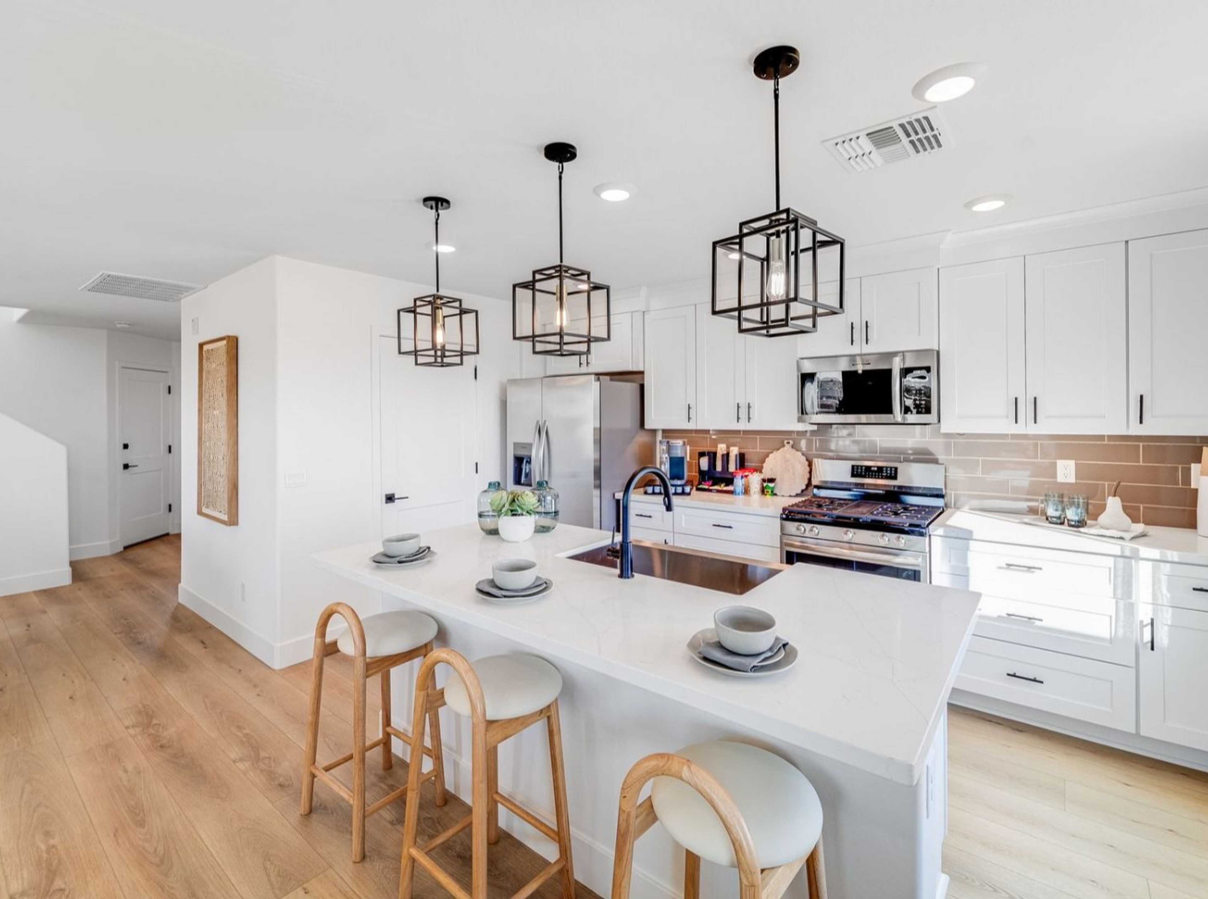 Spacious modern kitchen in Hidden Hills Prescott AZ by Davidson Homes with white cabinets, quartz island, bar stools, and hardwood floors