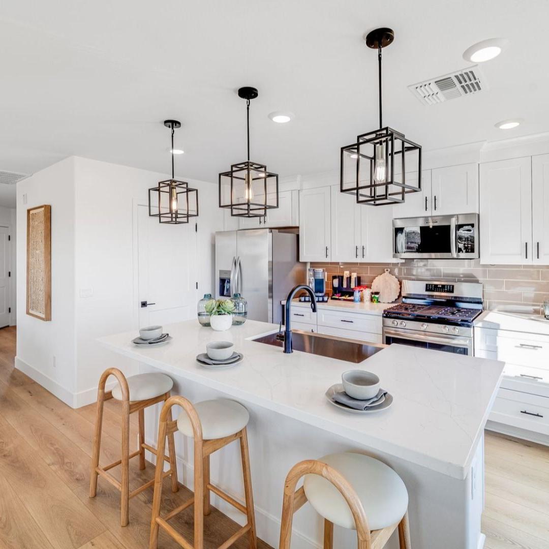 Spacious white kitchen at Senator Cottages in Prescott AZ with quartz island, bar stools, pendant lights, and stainless appliances