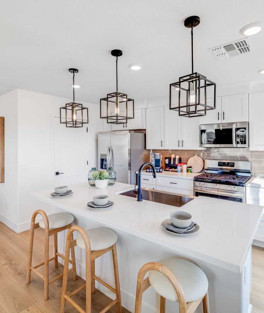 Spacious modern kitchen in Hidden Hills Prescott AZ by Davidson Homes with white cabinets, quartz island, bar stools, and hardwood floors