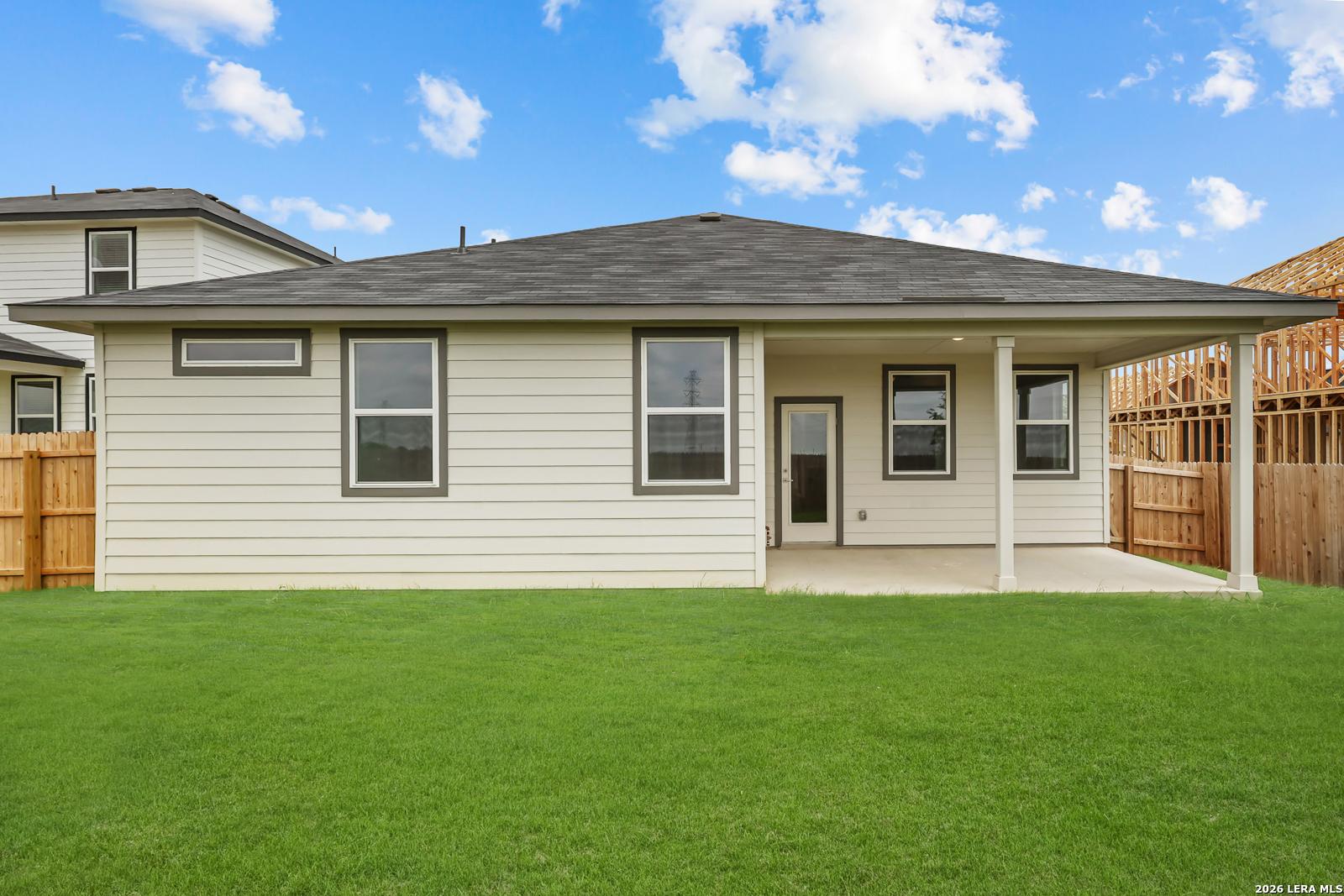 Covered back patio with large windows on beige-sided single-story home overlooking lush green lawn in Hickory Ridge, Elmendorf, Texas