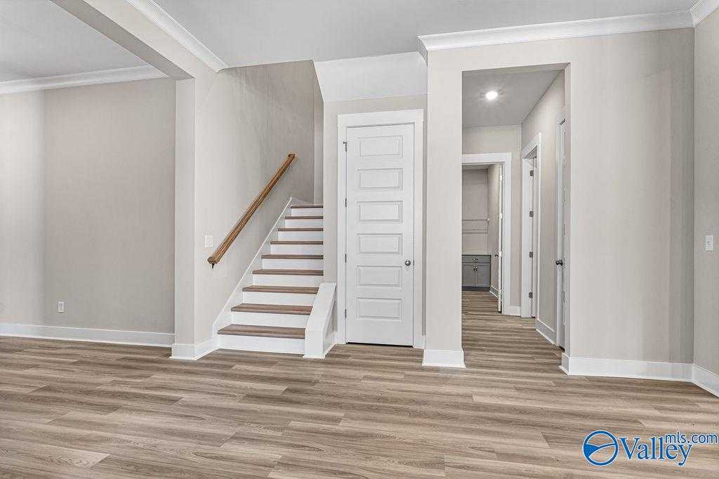 Elegant open entryway with wooden staircase, white doors, and light gray walls in Evermore Homes The Oxford, Owens Cross Roads, Alabama
